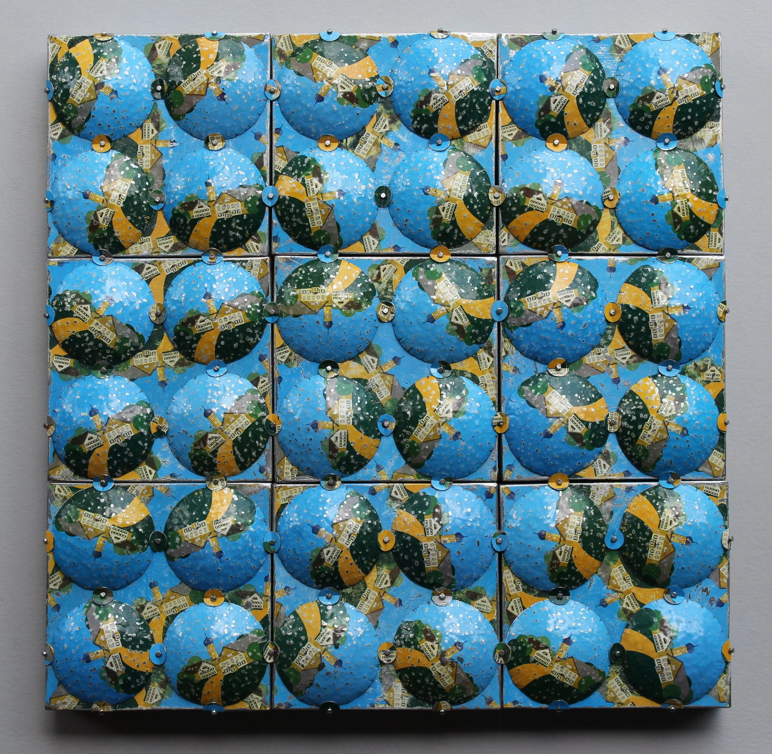 A wall installation composed of 16 reflective tiles, each featuring a blue, green, and yellow spherical design with small hardware images, arranged in a 4x4 grid.