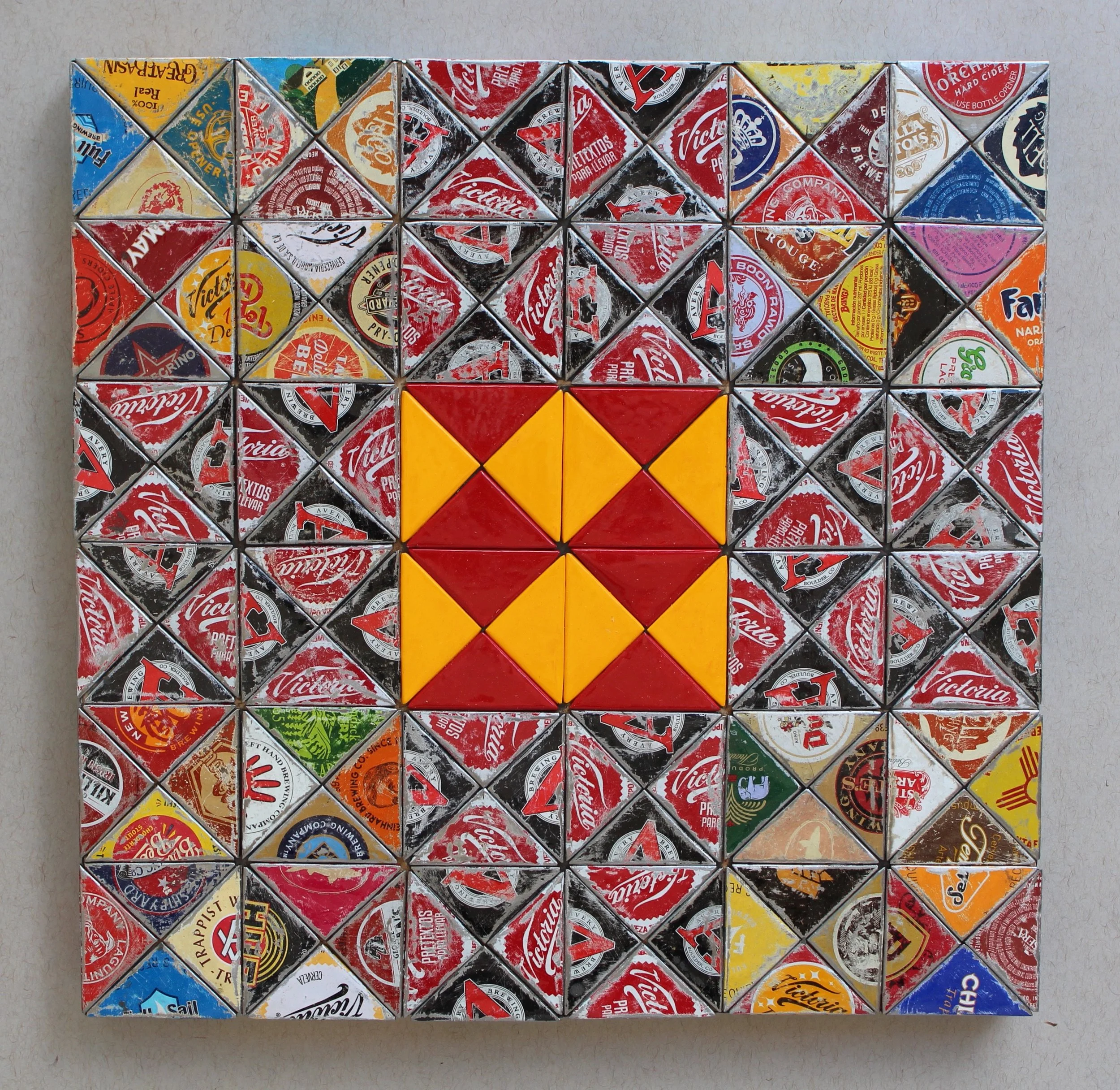 A mosaic made from crushed and cut beverage can tops, with a central pattern of red and yellow triangles.
