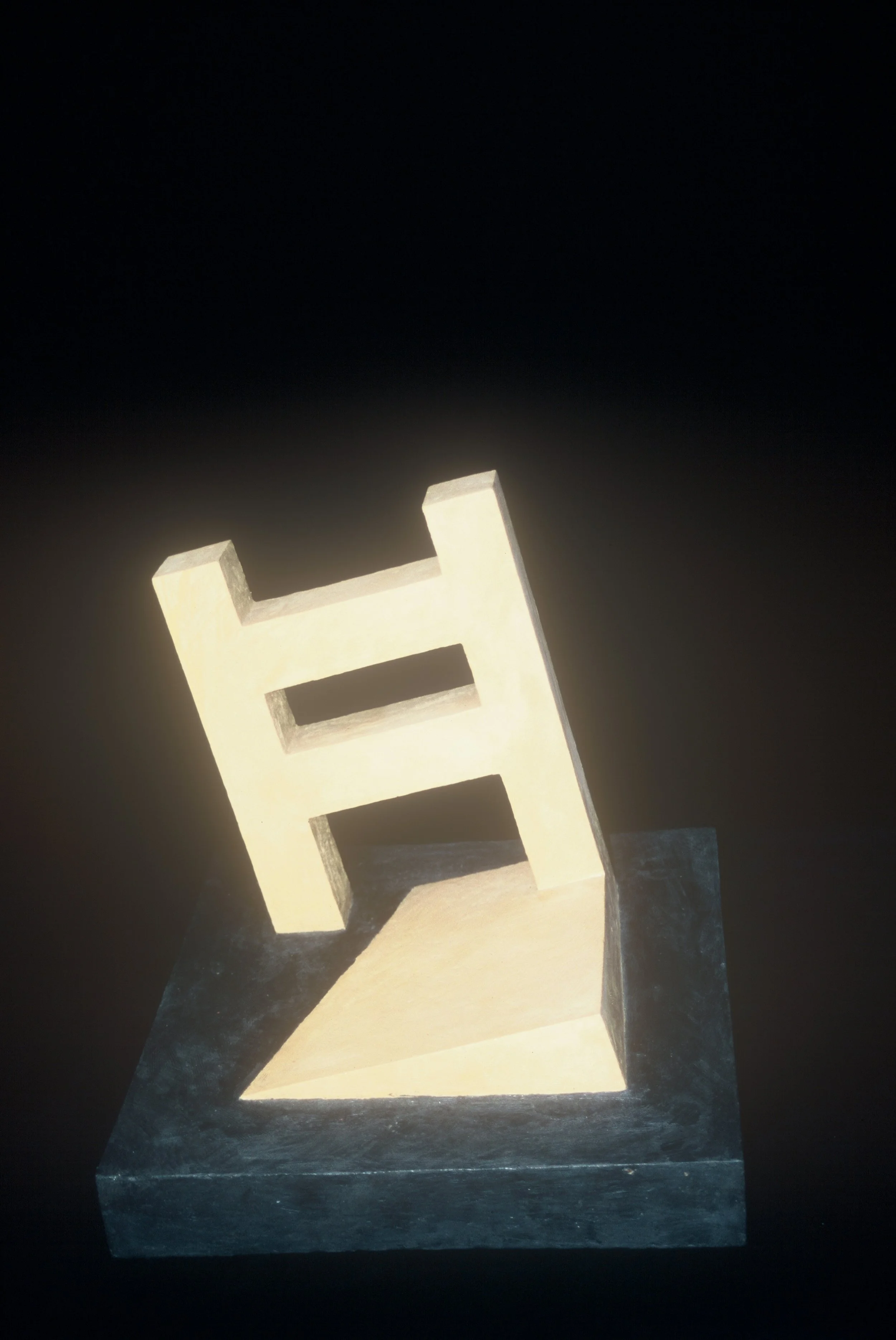 A geometric, abstract sculpture resembling the letter 'H', illuminated against a dark background.