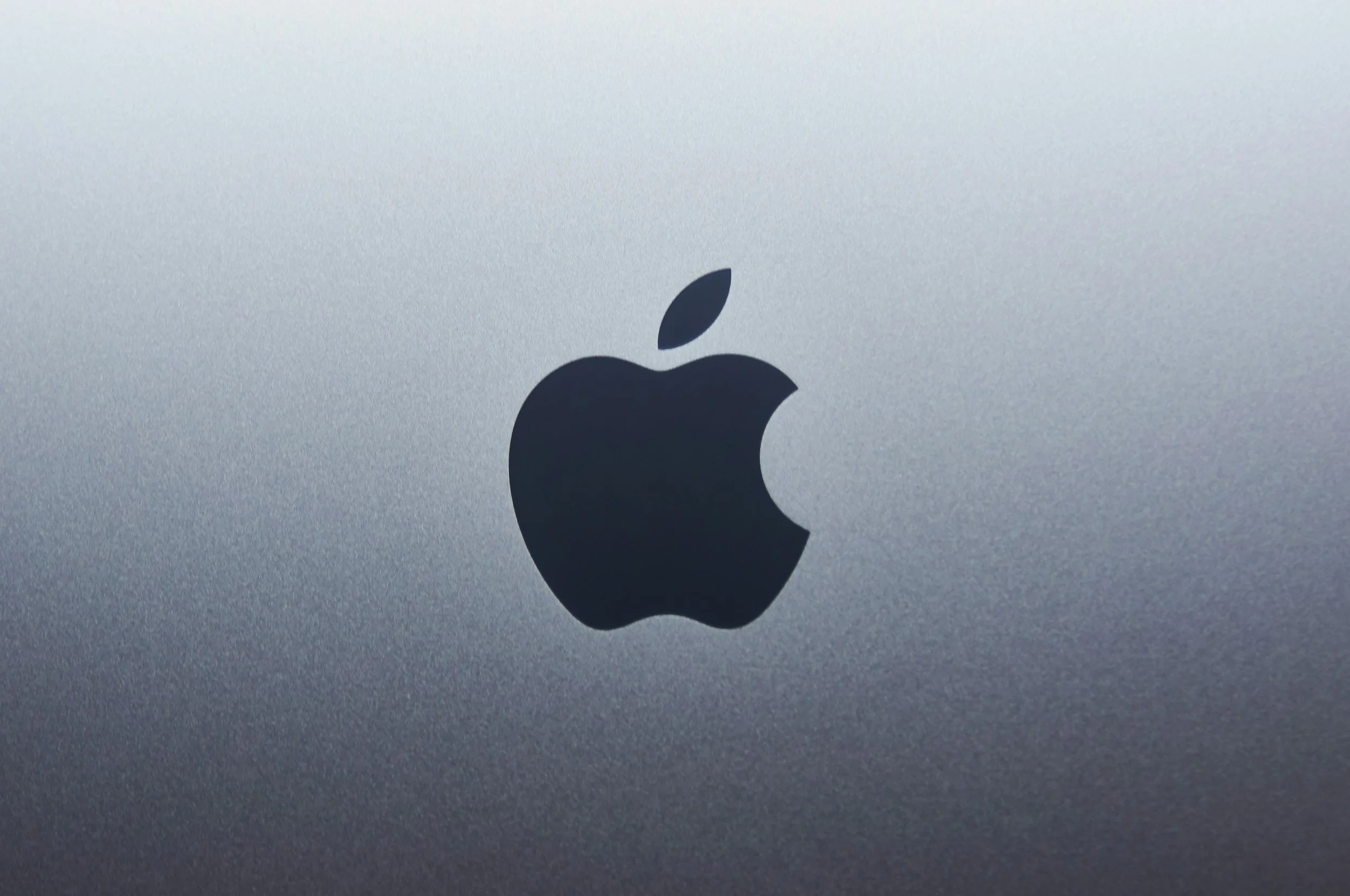 Close-up of a black Apple logo on a silver metallic surface.