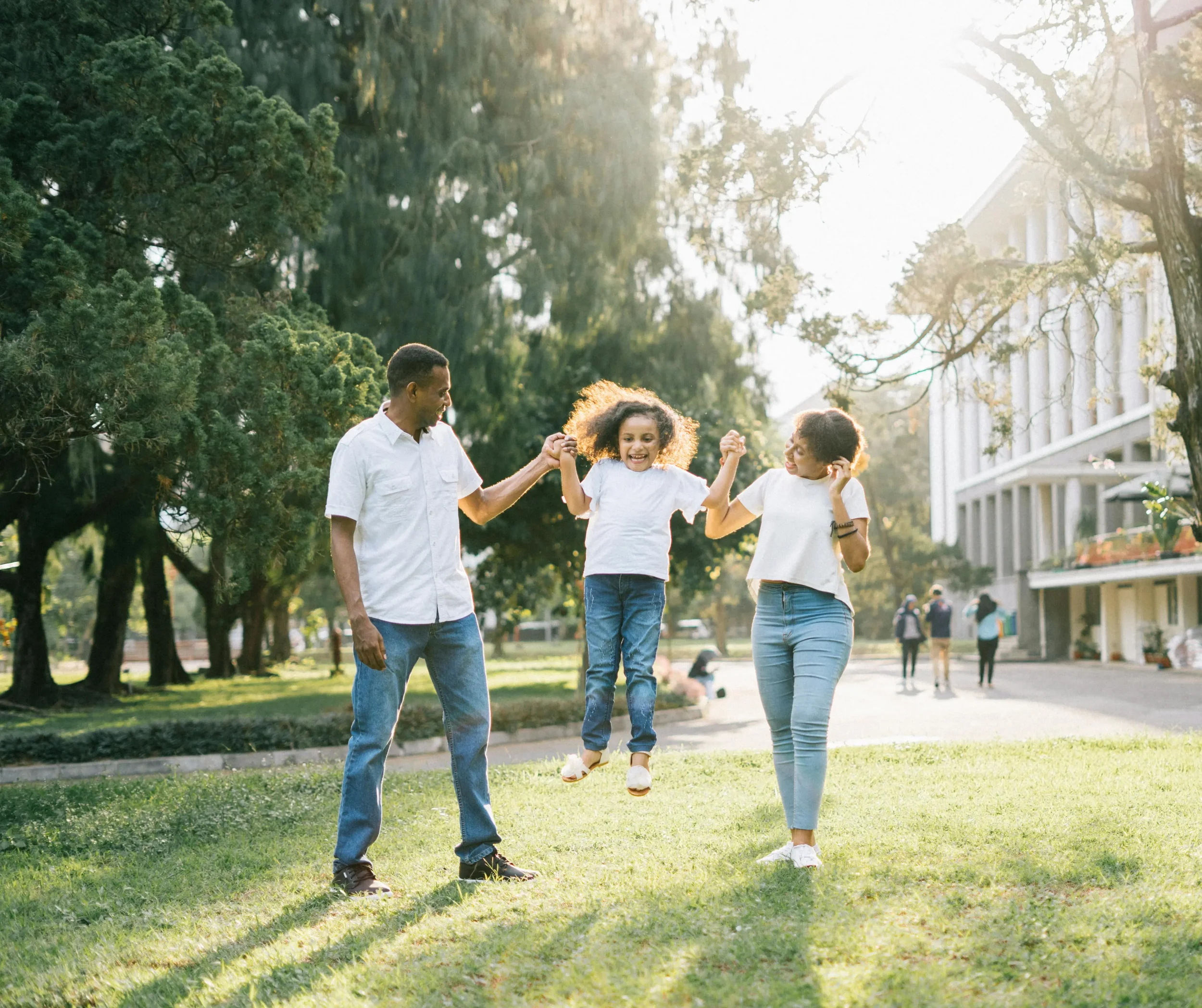A family with two parents and a daughter playing on the grass in a park during the late afternoon.