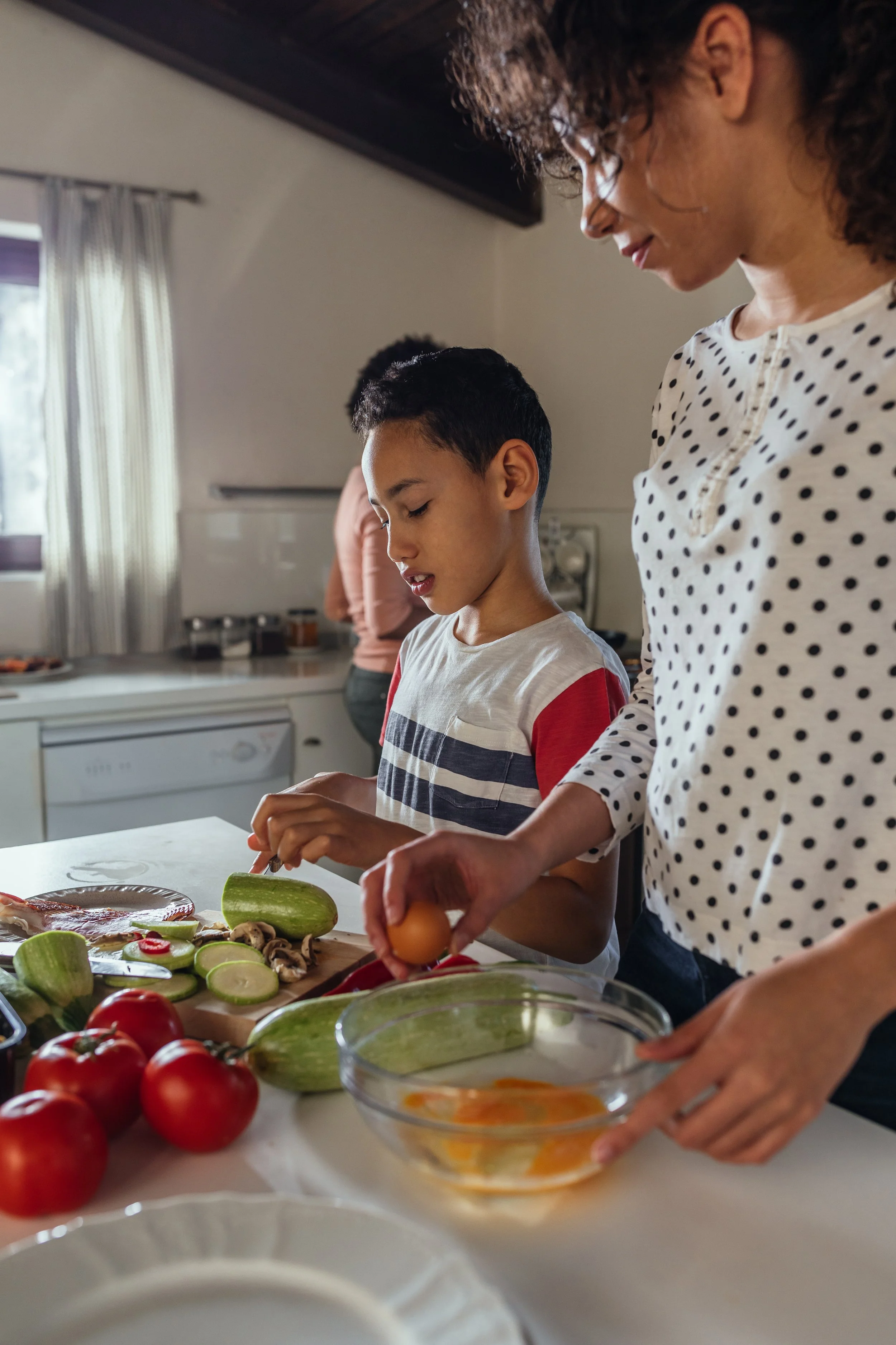 A woman and boy preparing vegetables and eggs in a kitchen.