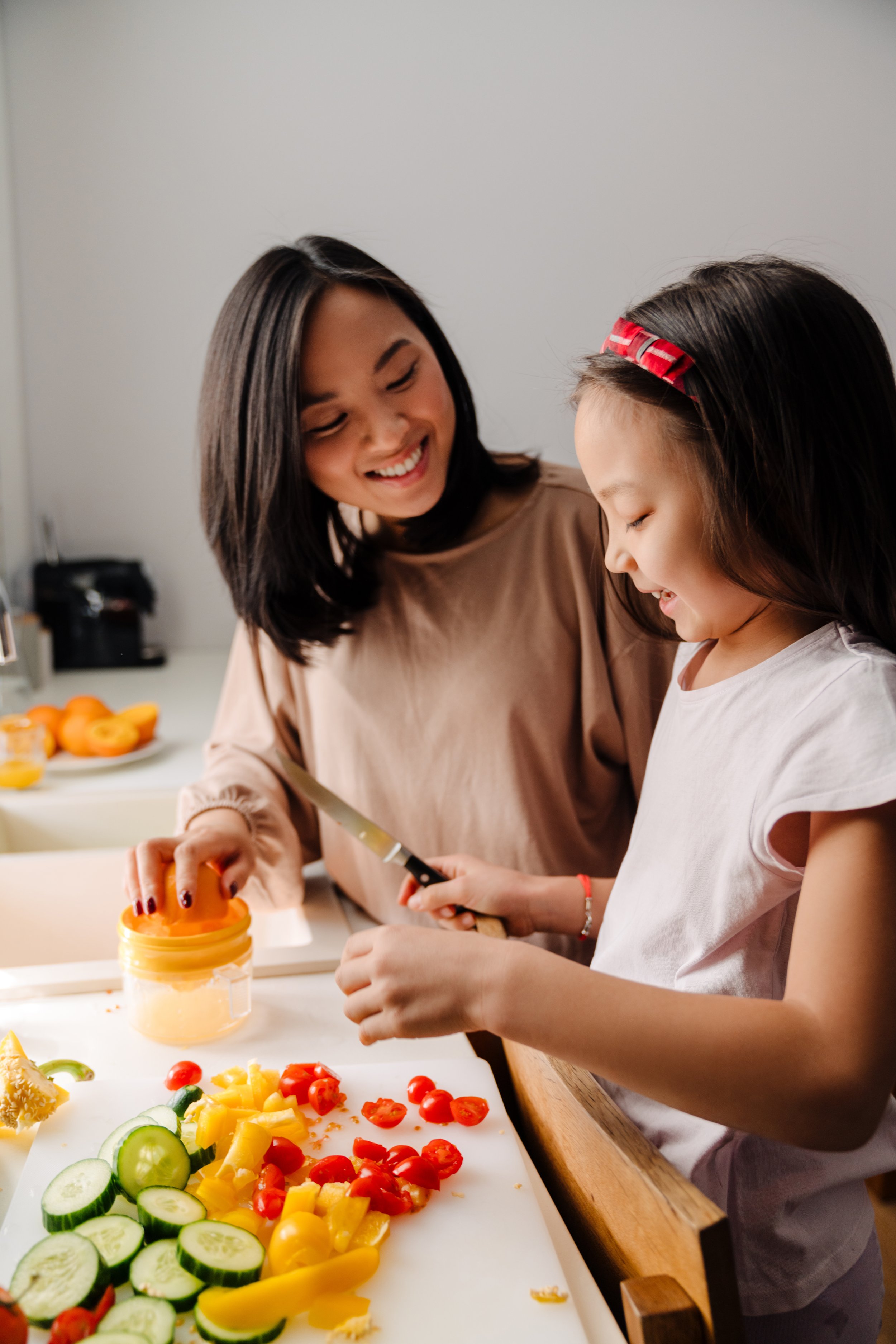 A woman and young girl preparing food together, chopping vegetables and smiling in a kitchen.