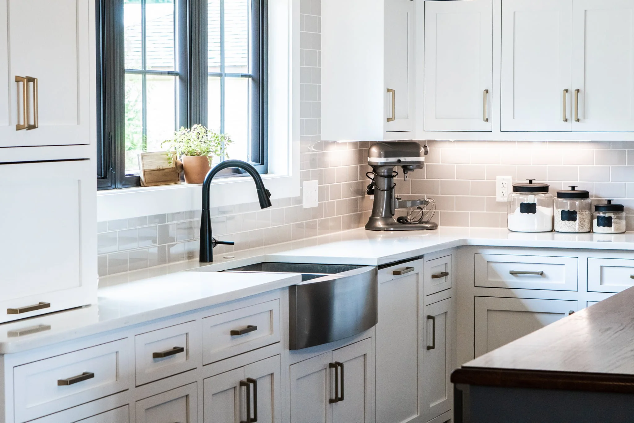 Modern kitchen with white cabinets, black faucet, window with black trim, houseplant, and countertop appliances.