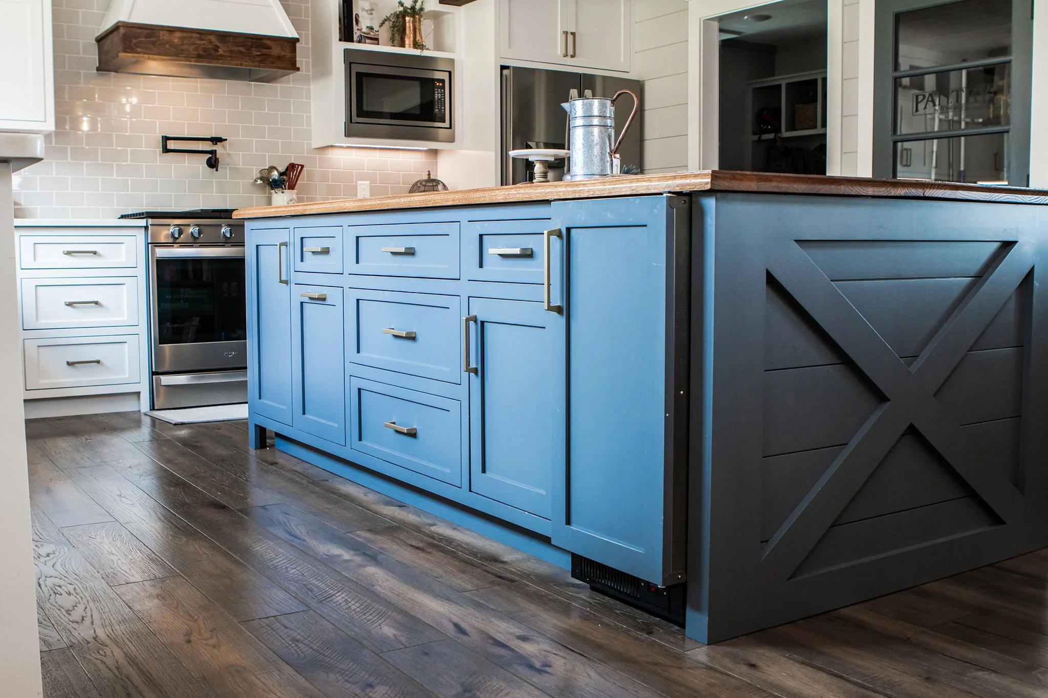 Kitchen with blue island, white cabinetry, stainless steel appliances, wooden countertop, and dark wood flooring.