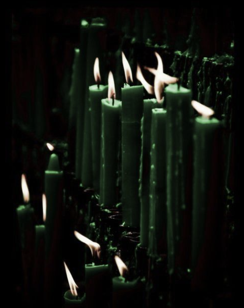 Green candles with burning flames in a dark setting.
