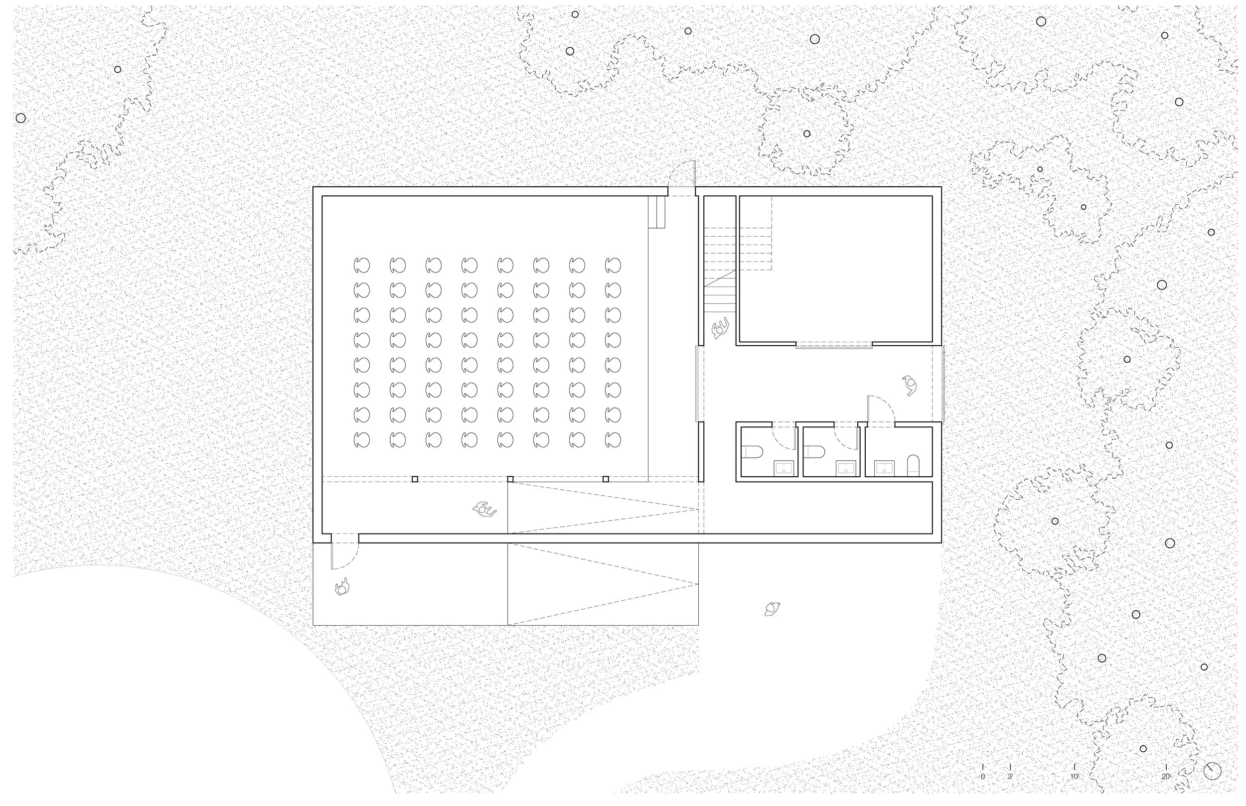Architectural floor plan of a building with an outdoor area, including a large seating area with rows of chairs, restrooms, and a staircase, surrounded by landscaped terrain with trees.