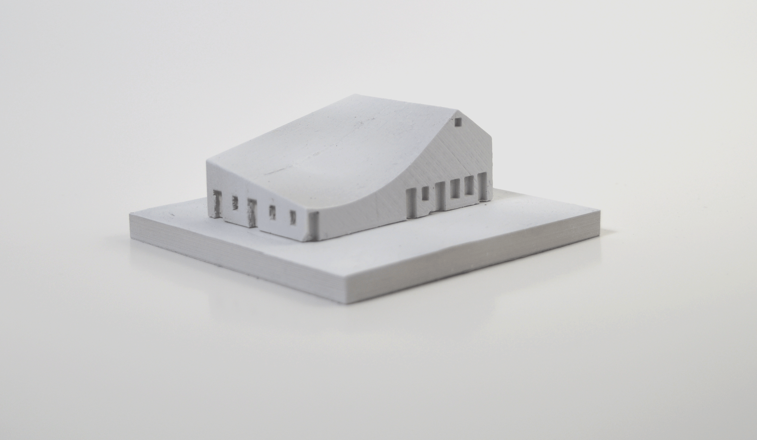 White architectural model of a modern building with a curved roof and multiple rectangular windows on a white base.