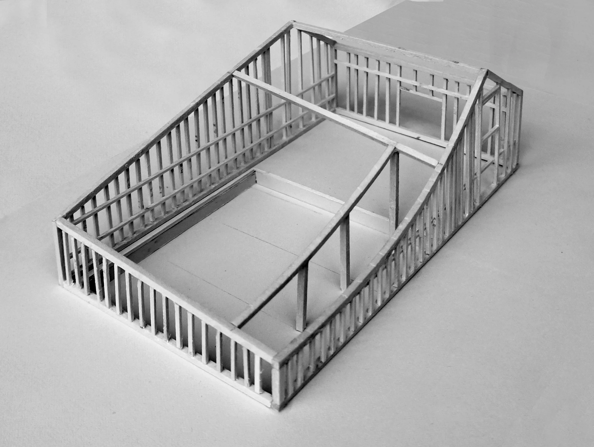 A black and white architectural model of a building with a rectangular layout, open roof, and interior walls, placed on a flat surface.