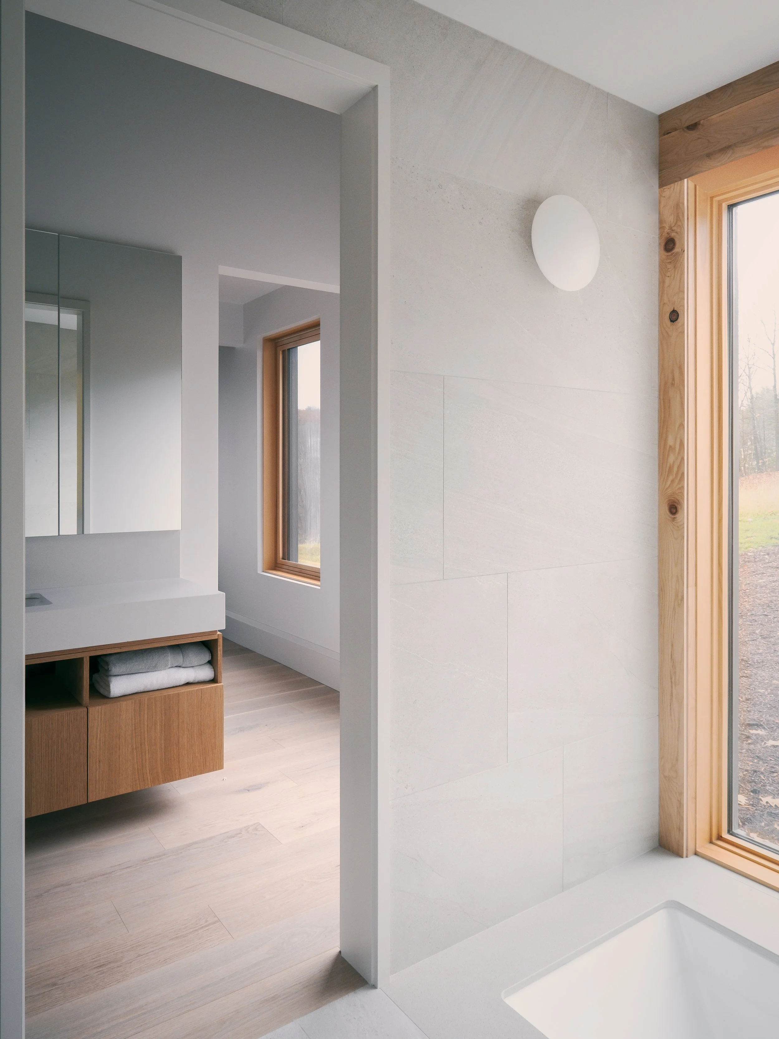 Modern bathroom with a large window, light wooden trim, and a white bathtub.