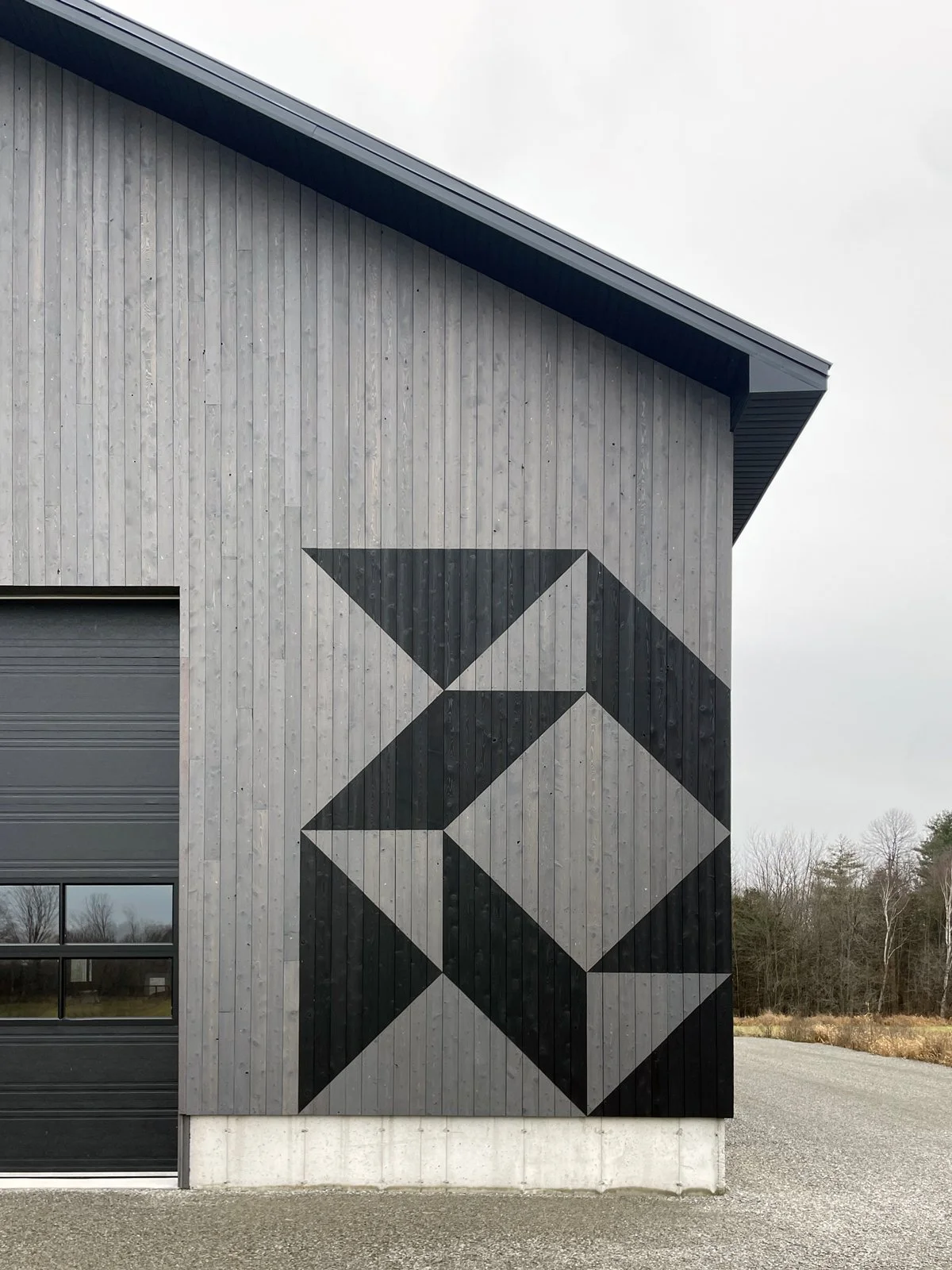 A modern building with gray wooden exterior walls and geometric black and gray artwork on the side.