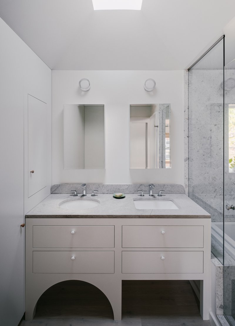 Modern bathroom with white vanity, double sinks, mirrors, and a glass-enclosed shower.