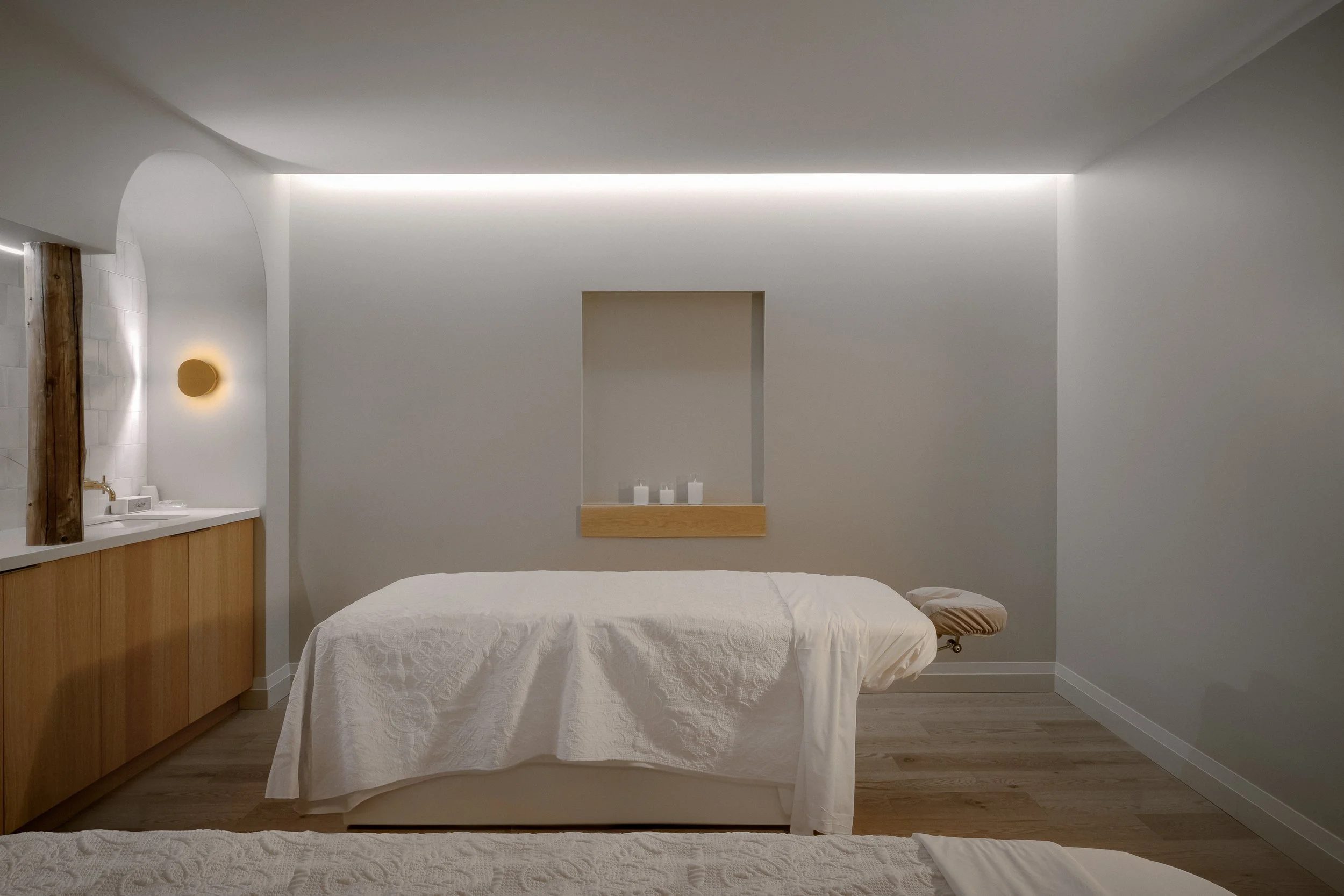 A minimalist massage room with a massage table, neutral color scheme, soft lighting, and simple decor.