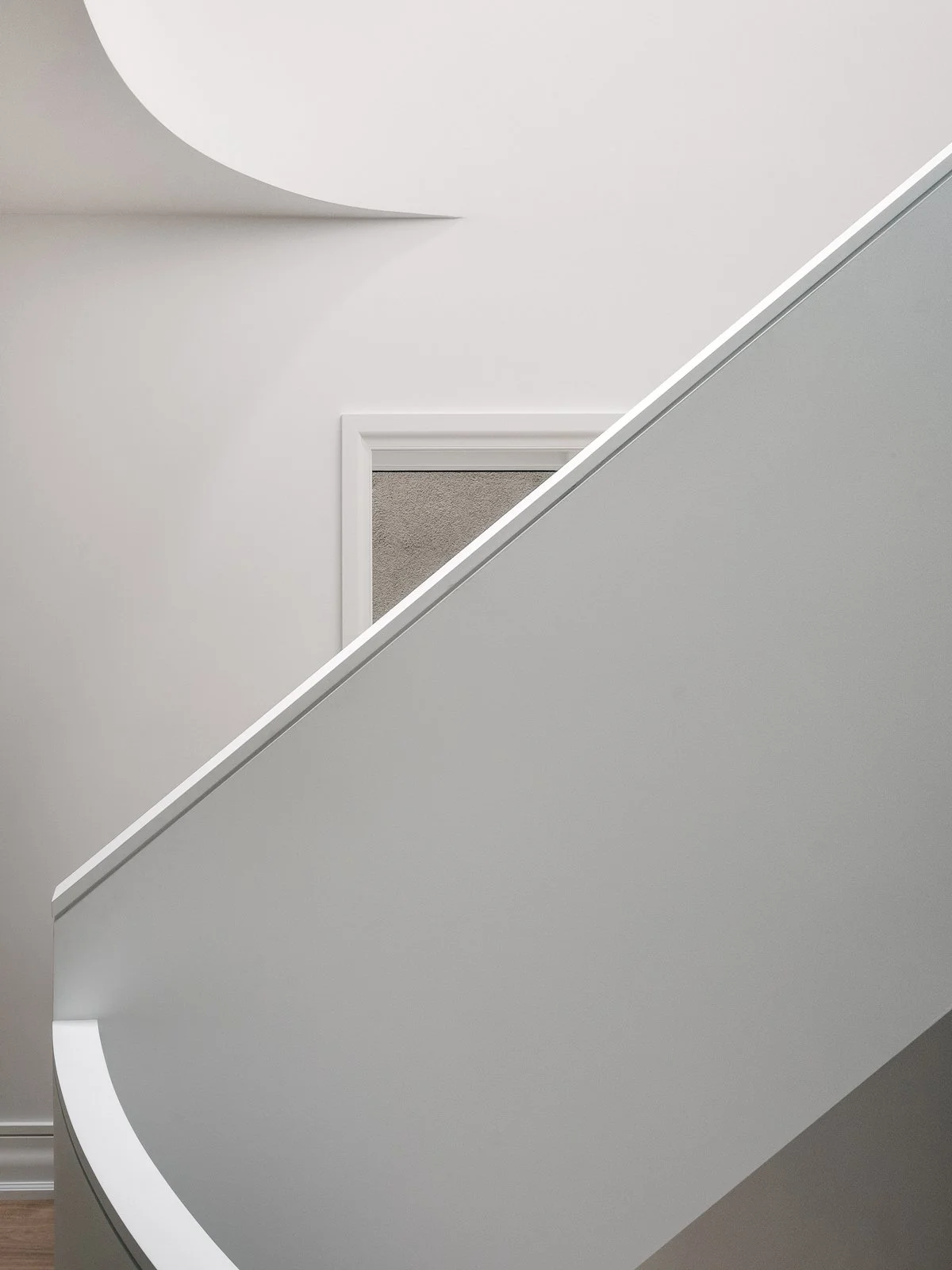 Close-up of a modern staircase with grey walls and a beige carpeted door in the background.