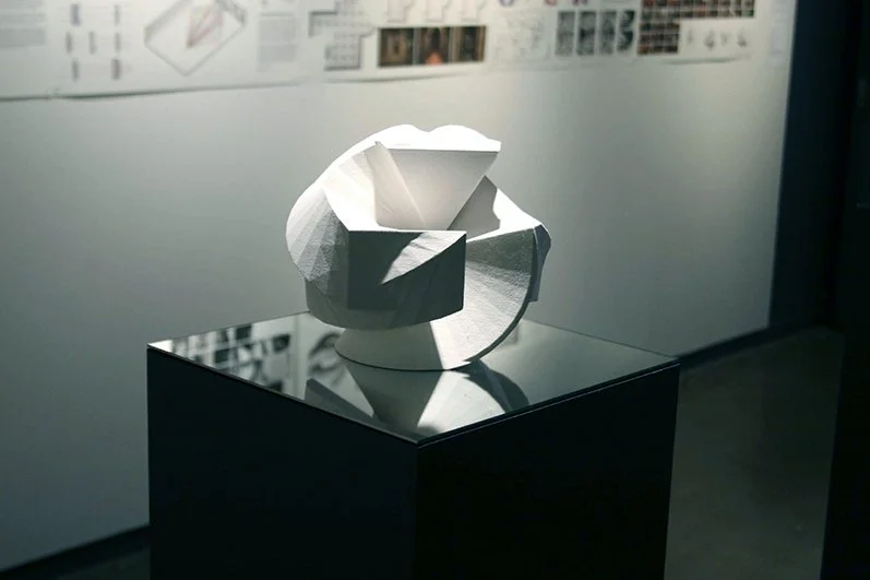 Modern abstract sculpture with geometric shapes on a reflective black pedestal in an art gallery.