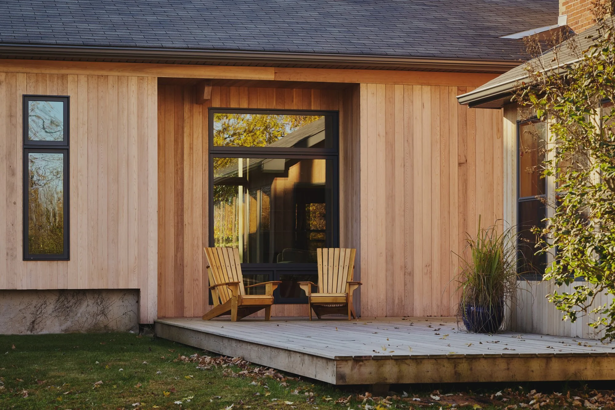 A wooden house with a deck, two wooden chairs, and a potted plant outside.