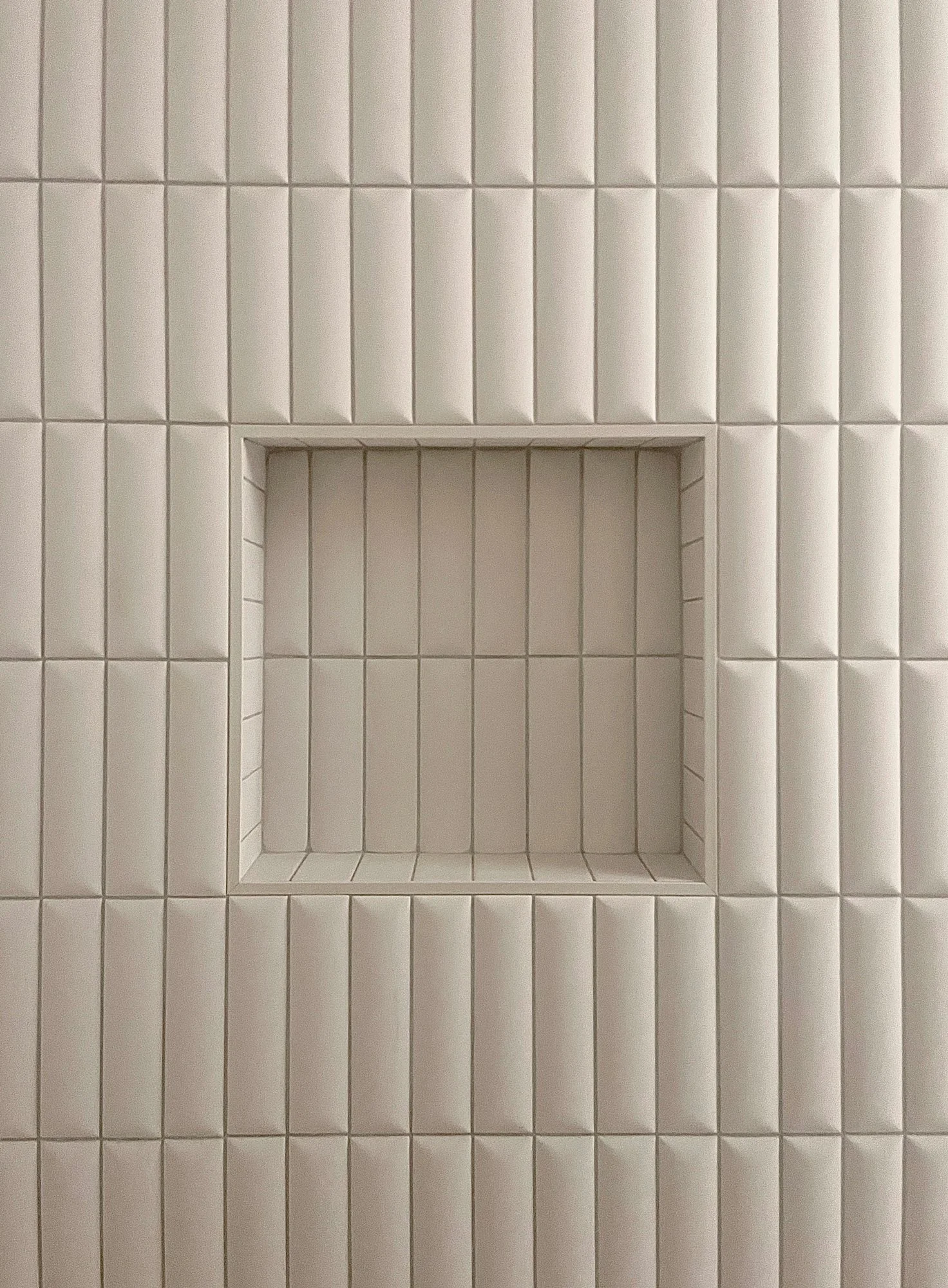 Close-up of a recessed square shelf built into a wall of white rectangular tiles.