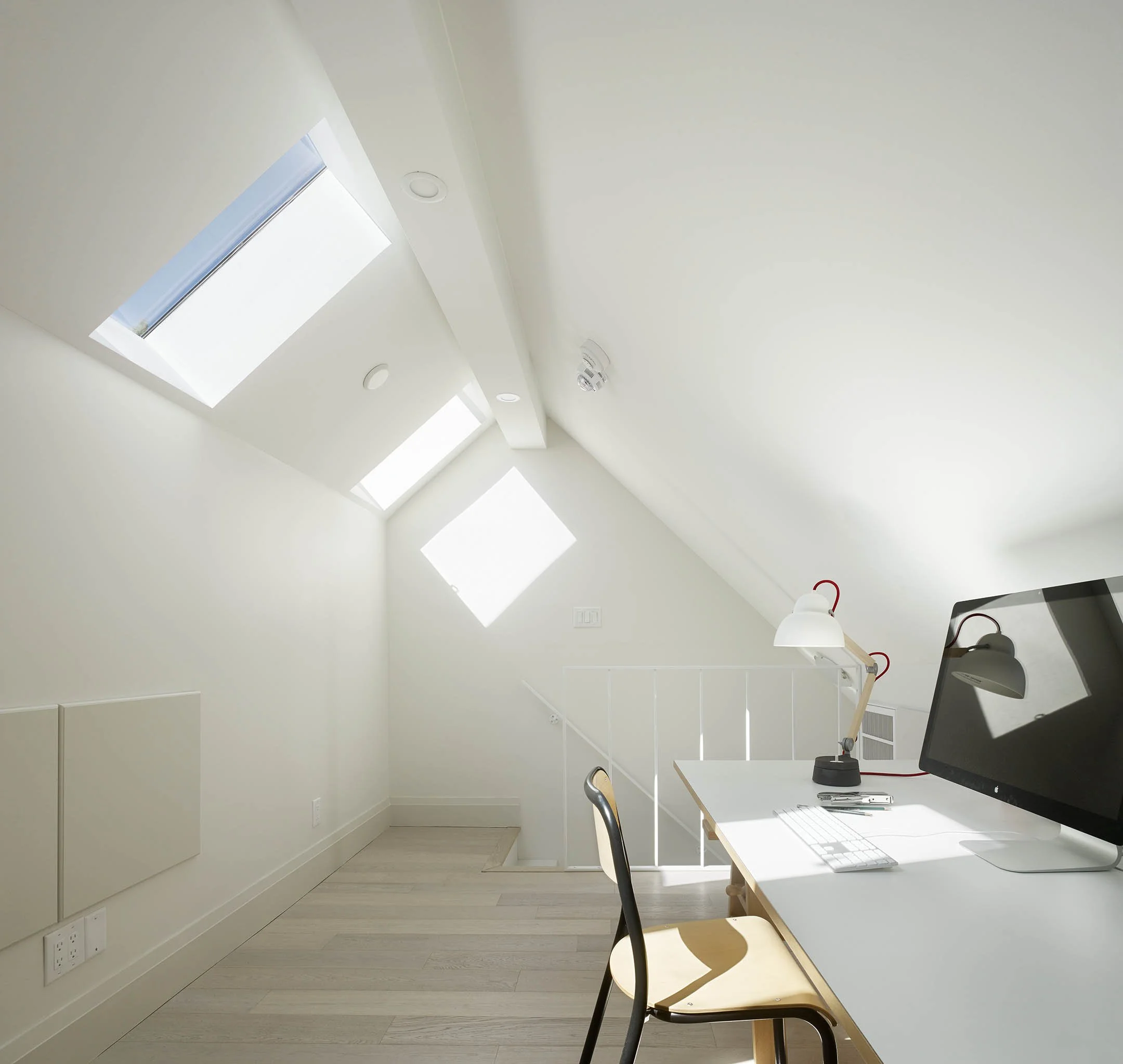 Bright white attic office with desk, computer, and lamp, illuminated by three skylight windows.