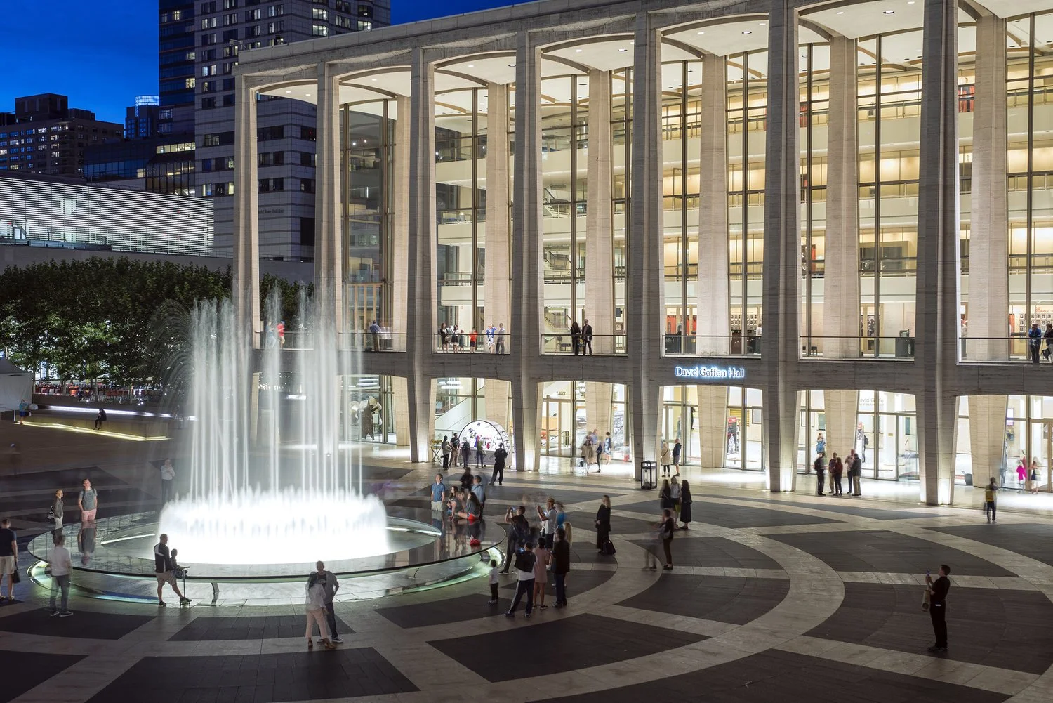 Night view of David Geffen Hall building with people around and a water fountain in front.