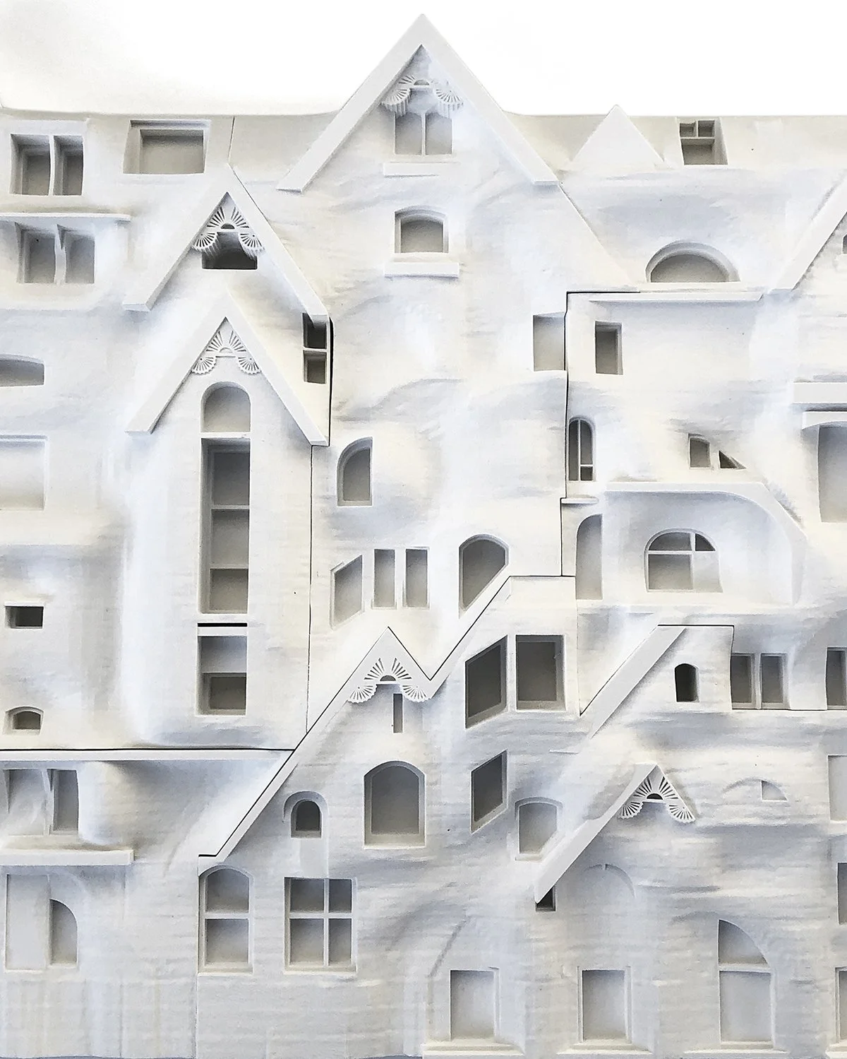 A detailed white architectural model of a house with multiple rooms and windows, featuring various geometric shapes and rooflines.