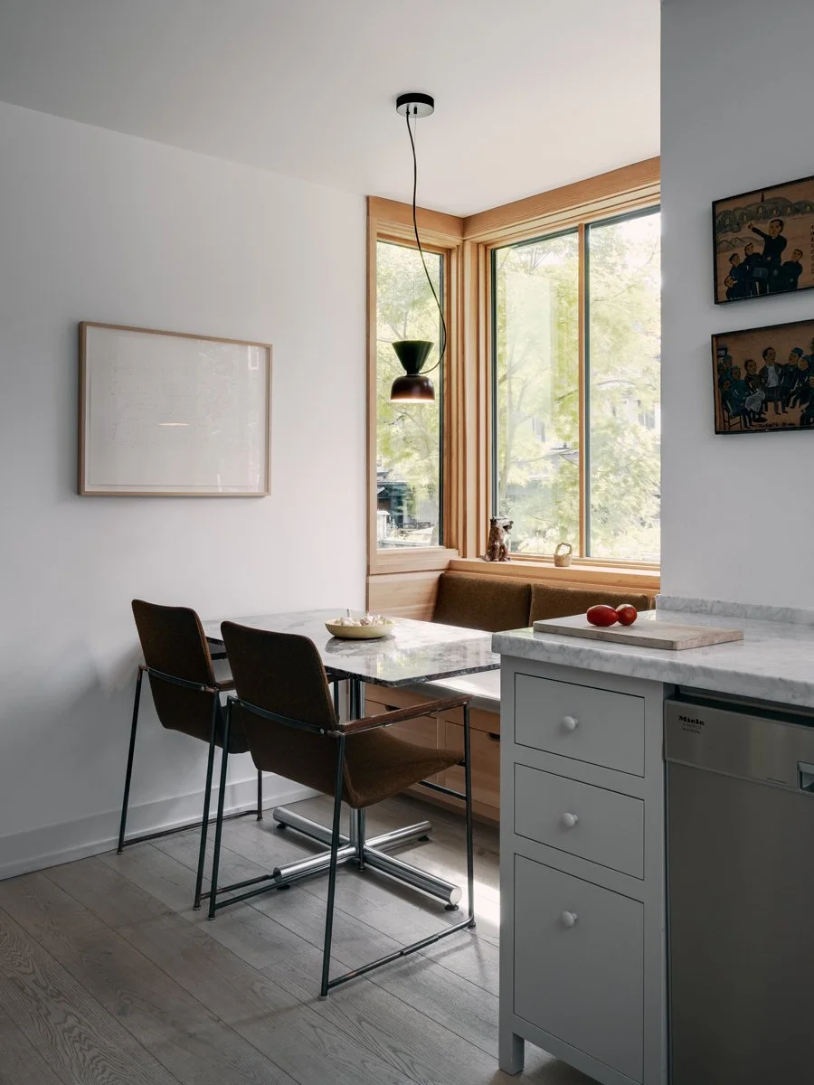 Modern kitchen with a marble dining table, two brown chairs, large window with wood trim, built-in bench, and hanging pendant light.