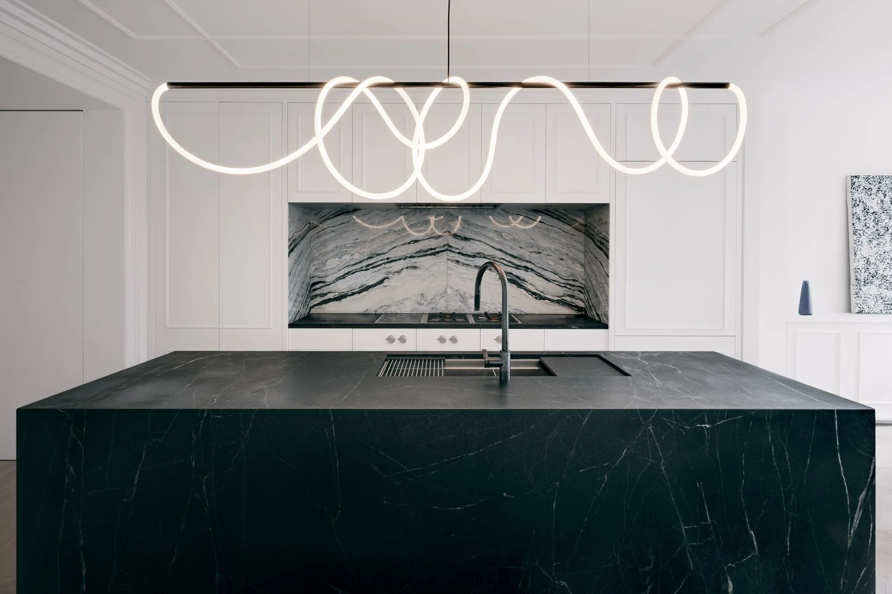 Modern kitchen with a black marble island, white cabinets, and a marble backsplash. Stylish white pendant lights hang above the island.
