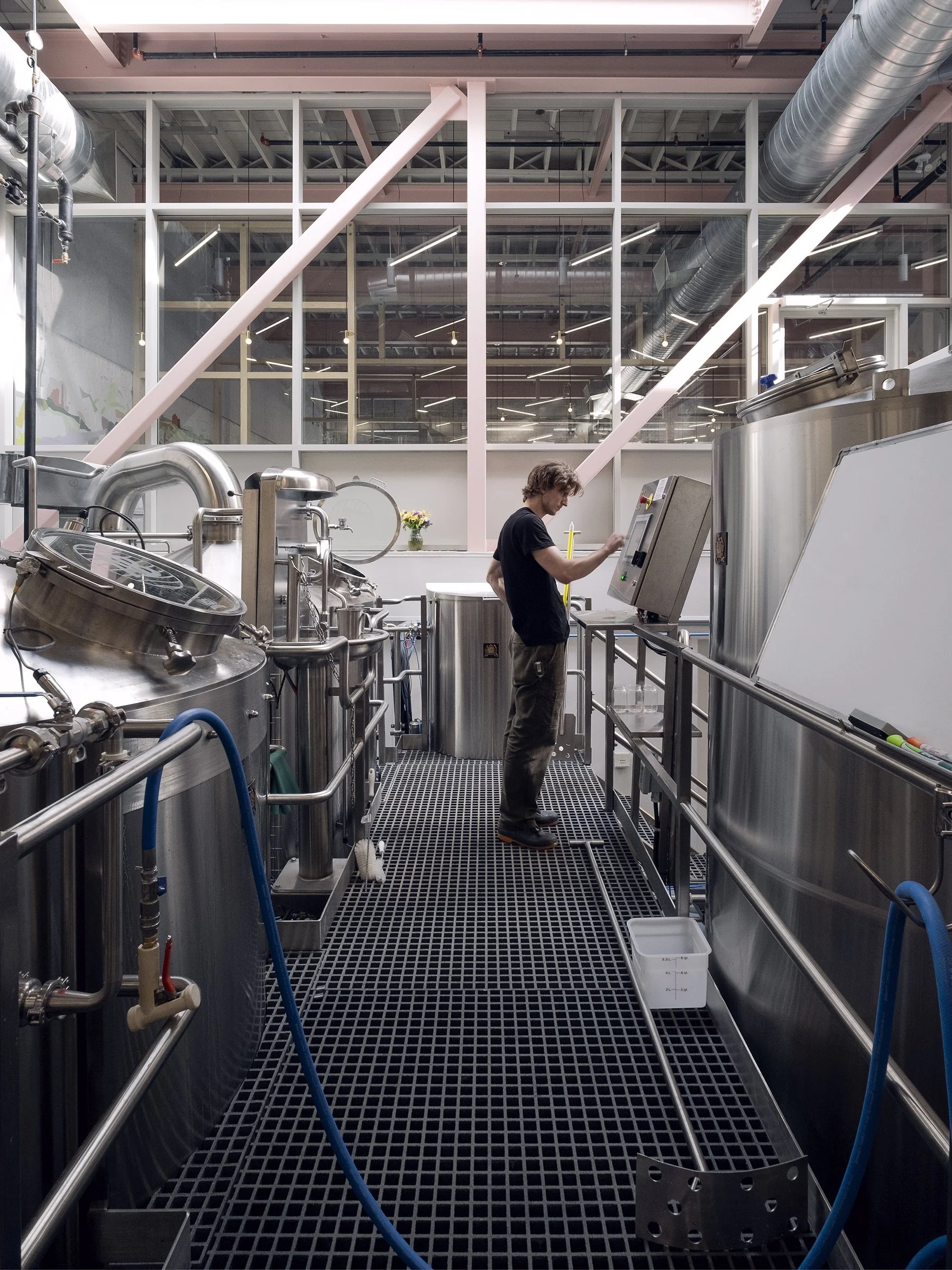 A man on a platform inspecting industrial brewing equipment in a brewery.