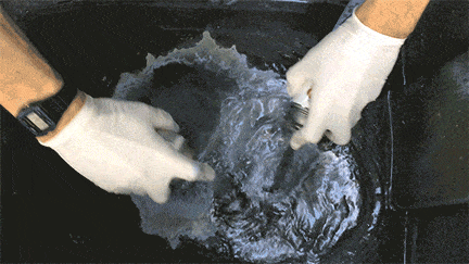 Person wearing gloves submerging hands in water, possibly washing or cleaning.