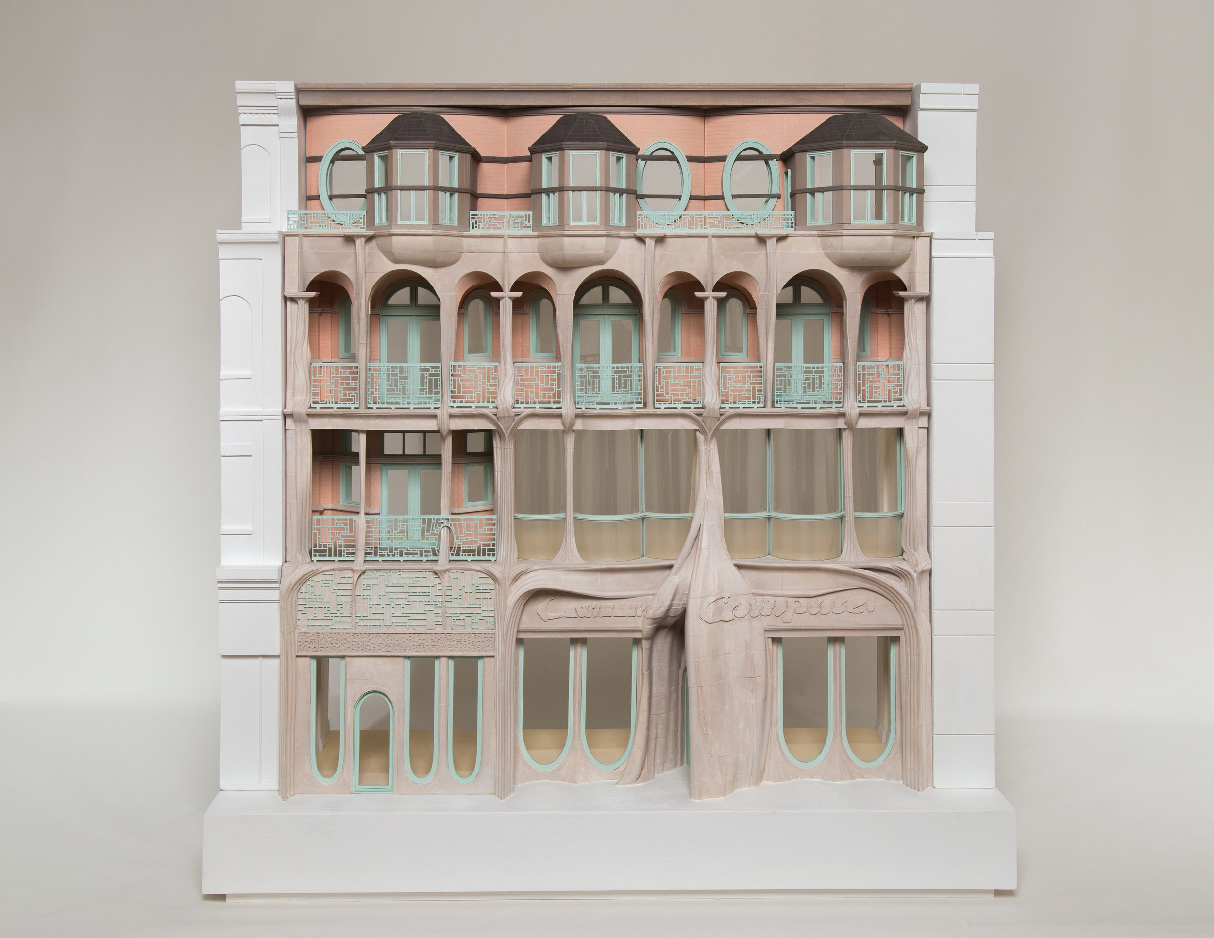 Architectural model of a multi-story building with ornate balconies and large windows, featuring pastel colors and intricate designs.