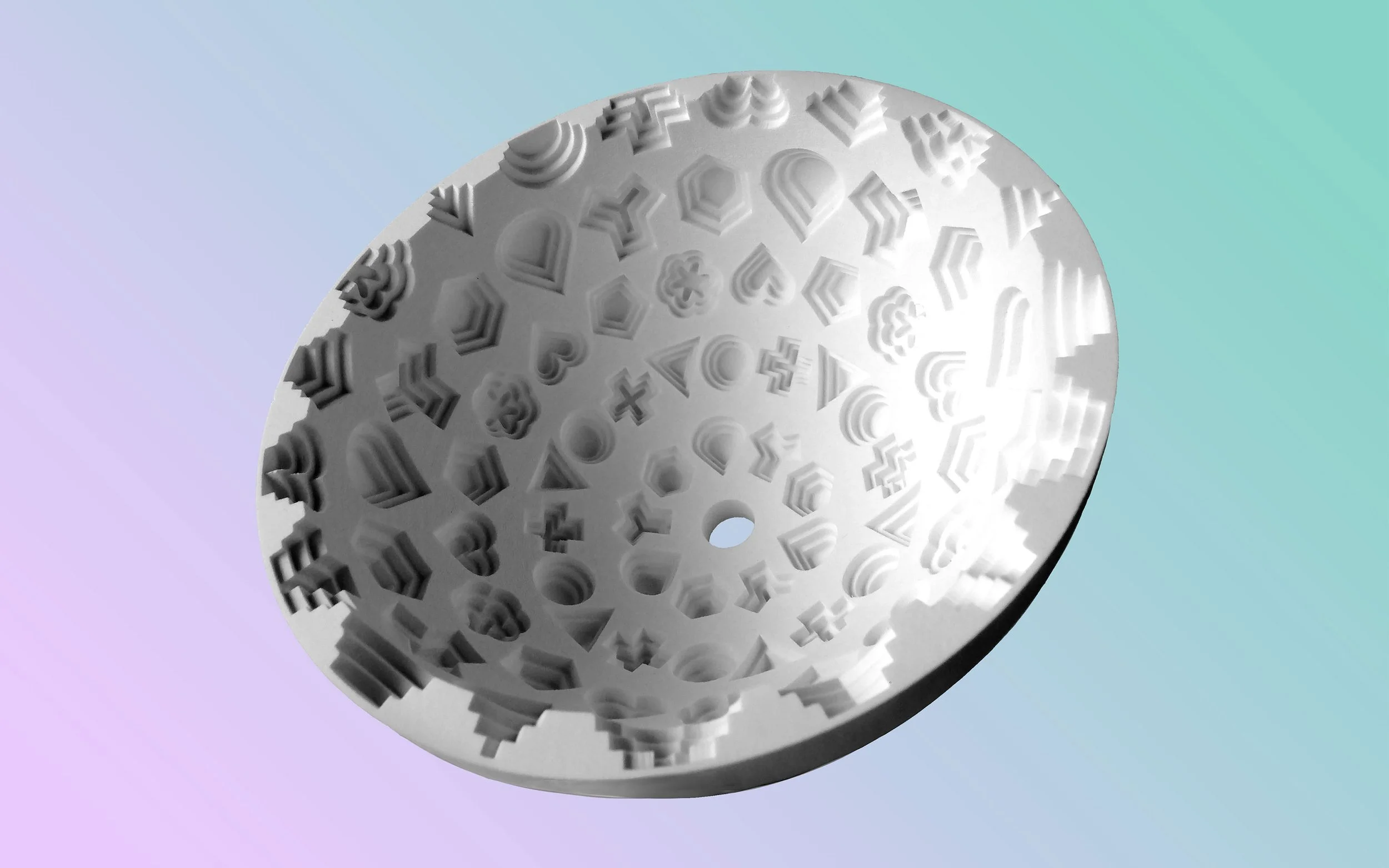 A round, white object with various geometric and symbolic cutouts and engravings, placed on a light gradient background.