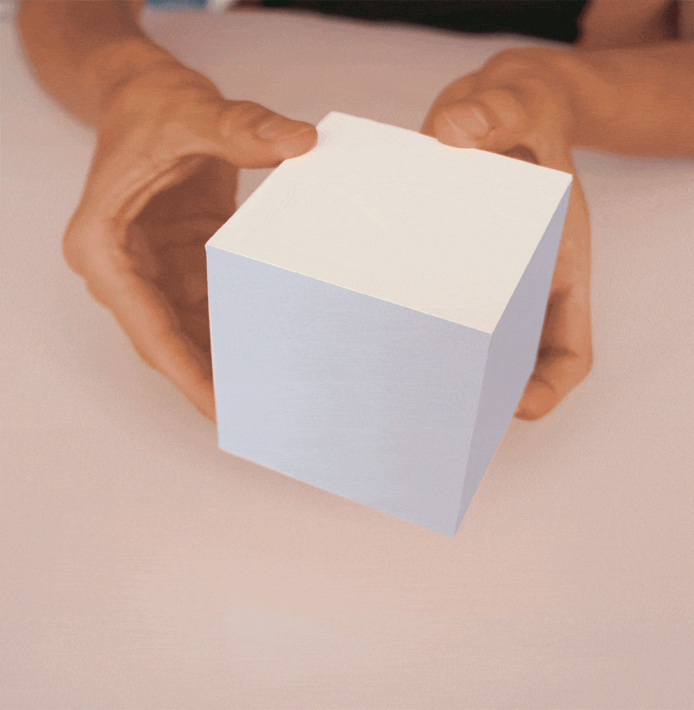 A person's hands holding a white cube against a light pink background.