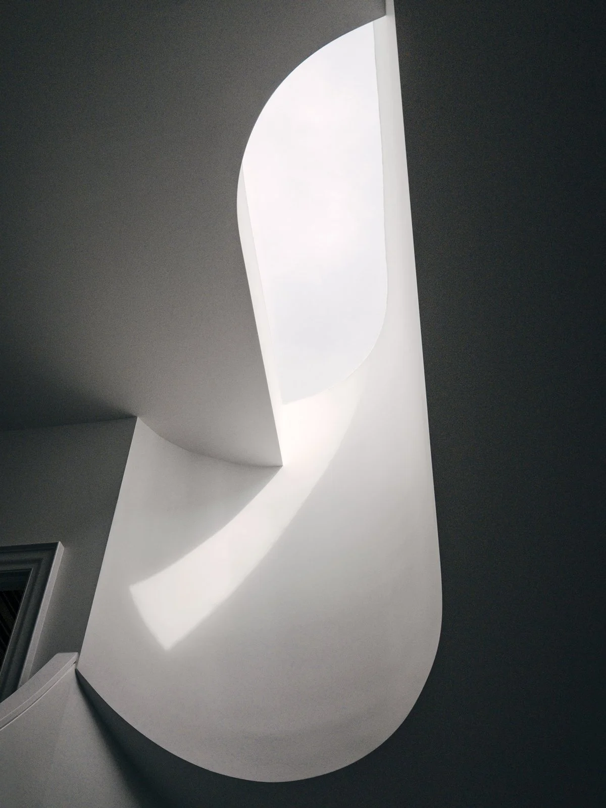 Modern abstract ceiling light fixture with curved white design and natural light shining through an opening.