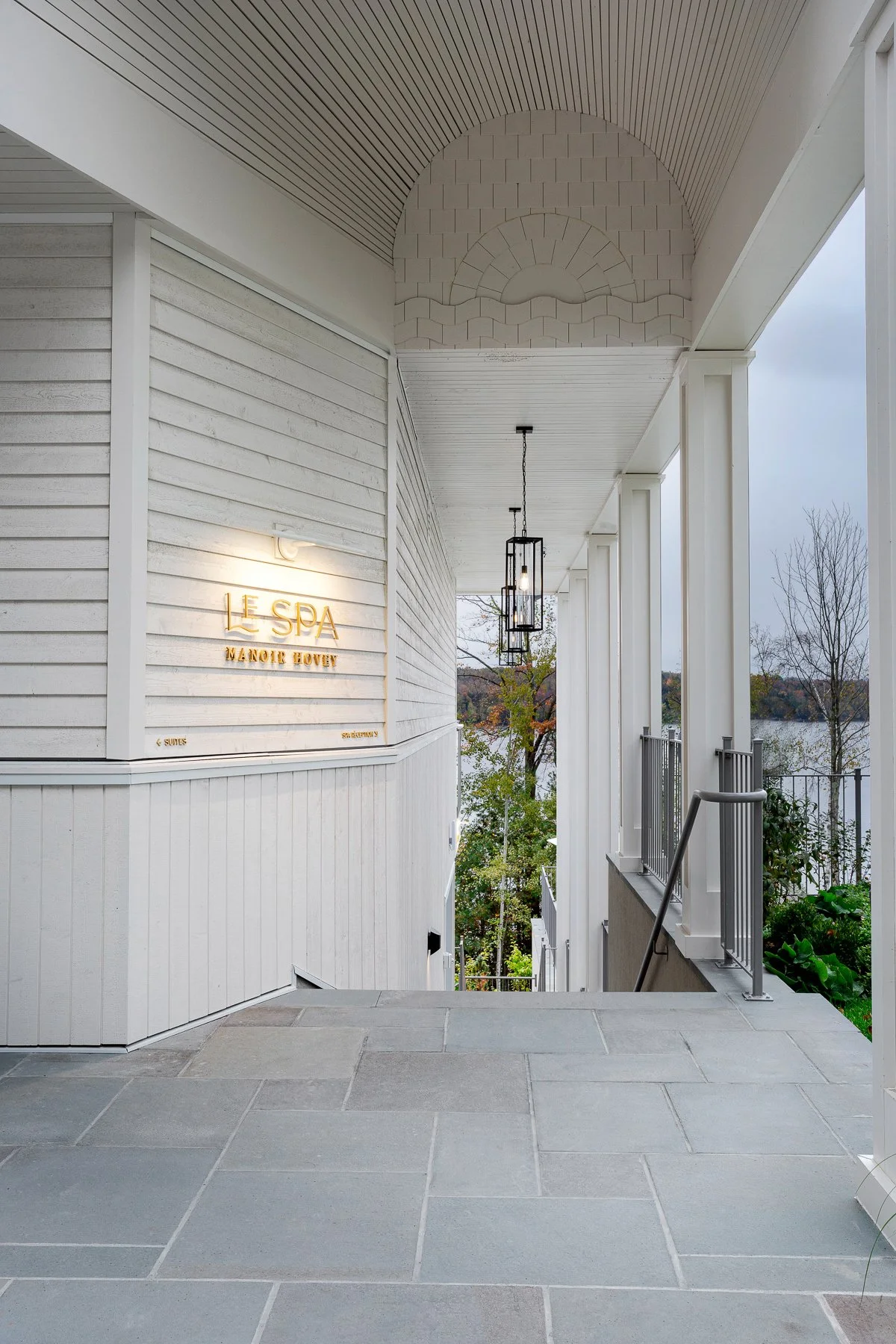 Exterior of a white spa building with a sign reading 'Le Spa Manoir Hovey' and a view of trees and a lake in the background.