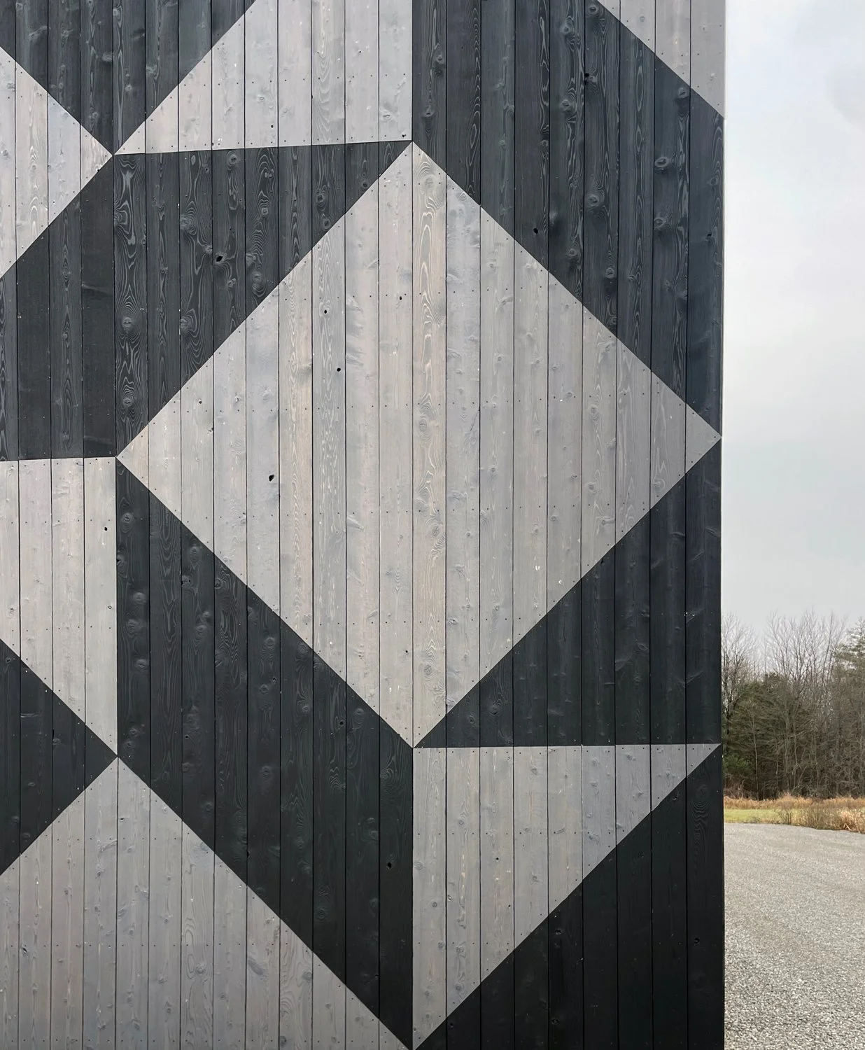 A large geometric mural painted on a wooden wall, featuring black, gray, and white shapes forming a three-dimensional cube pattern.