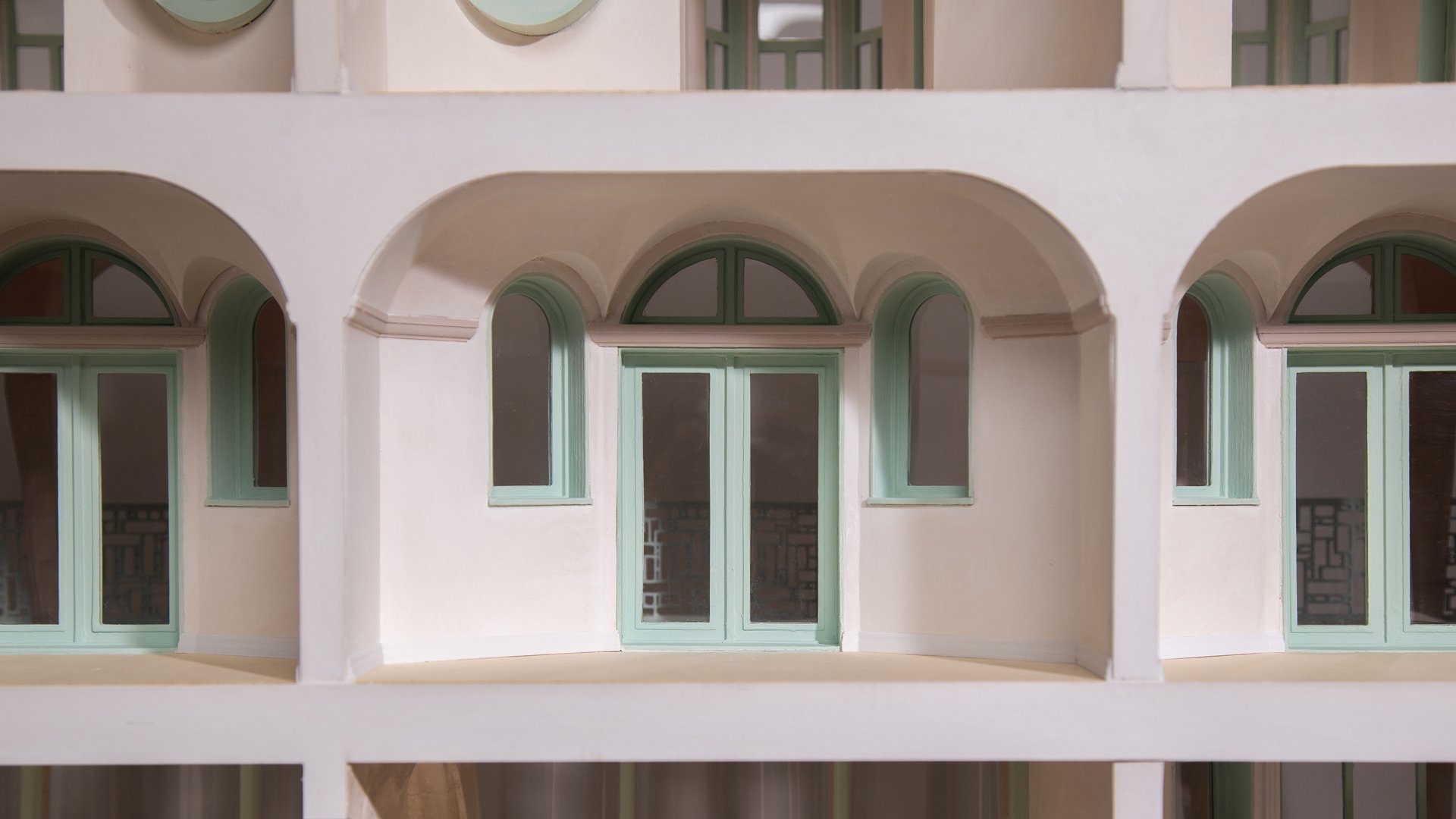 Architectural model of a building with white walls and arched windows with light green frames.