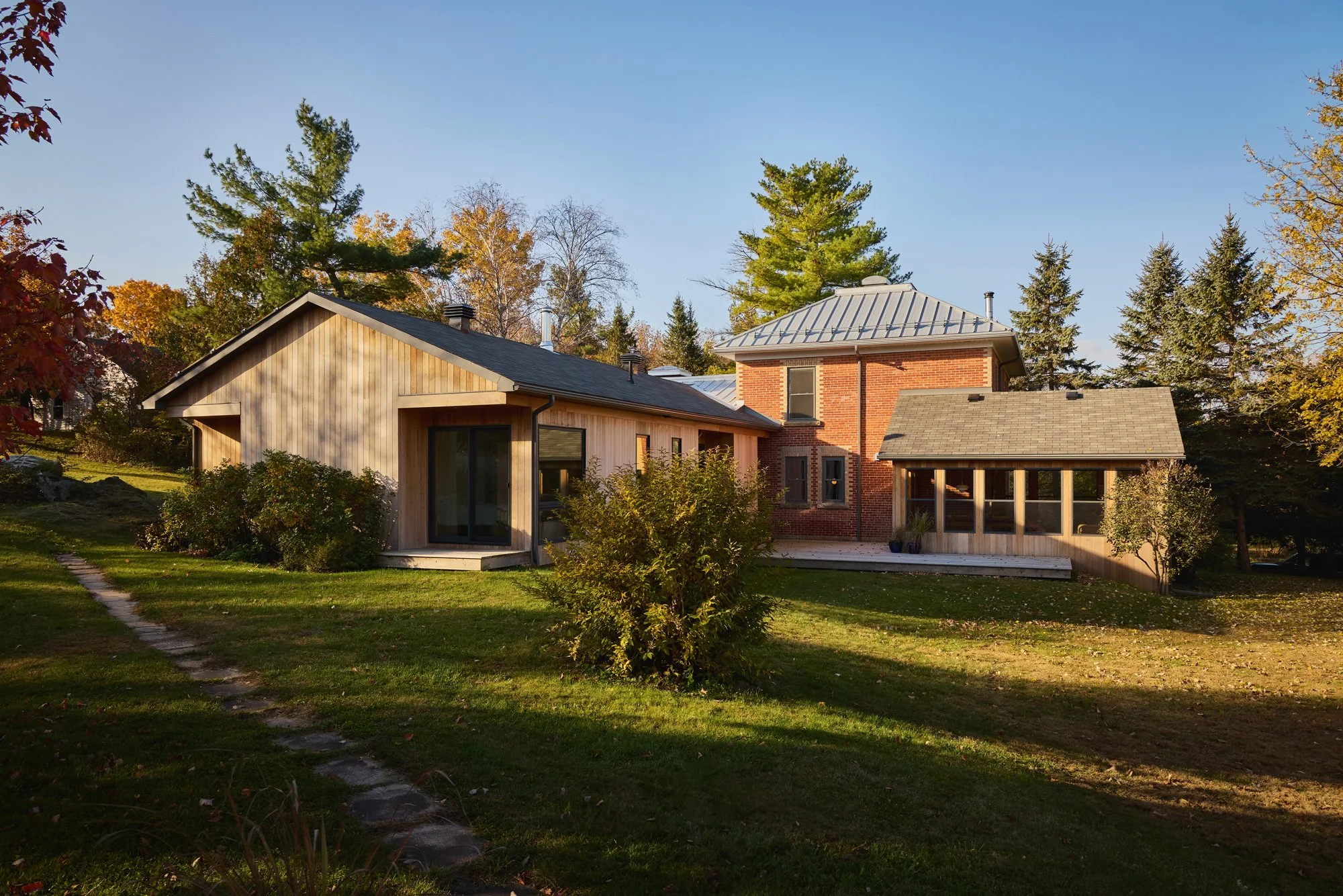 A modern residential house with a mix of wood and brick exterior, surrounded by trees and a well-maintained lawn, during daytime with clear skies.