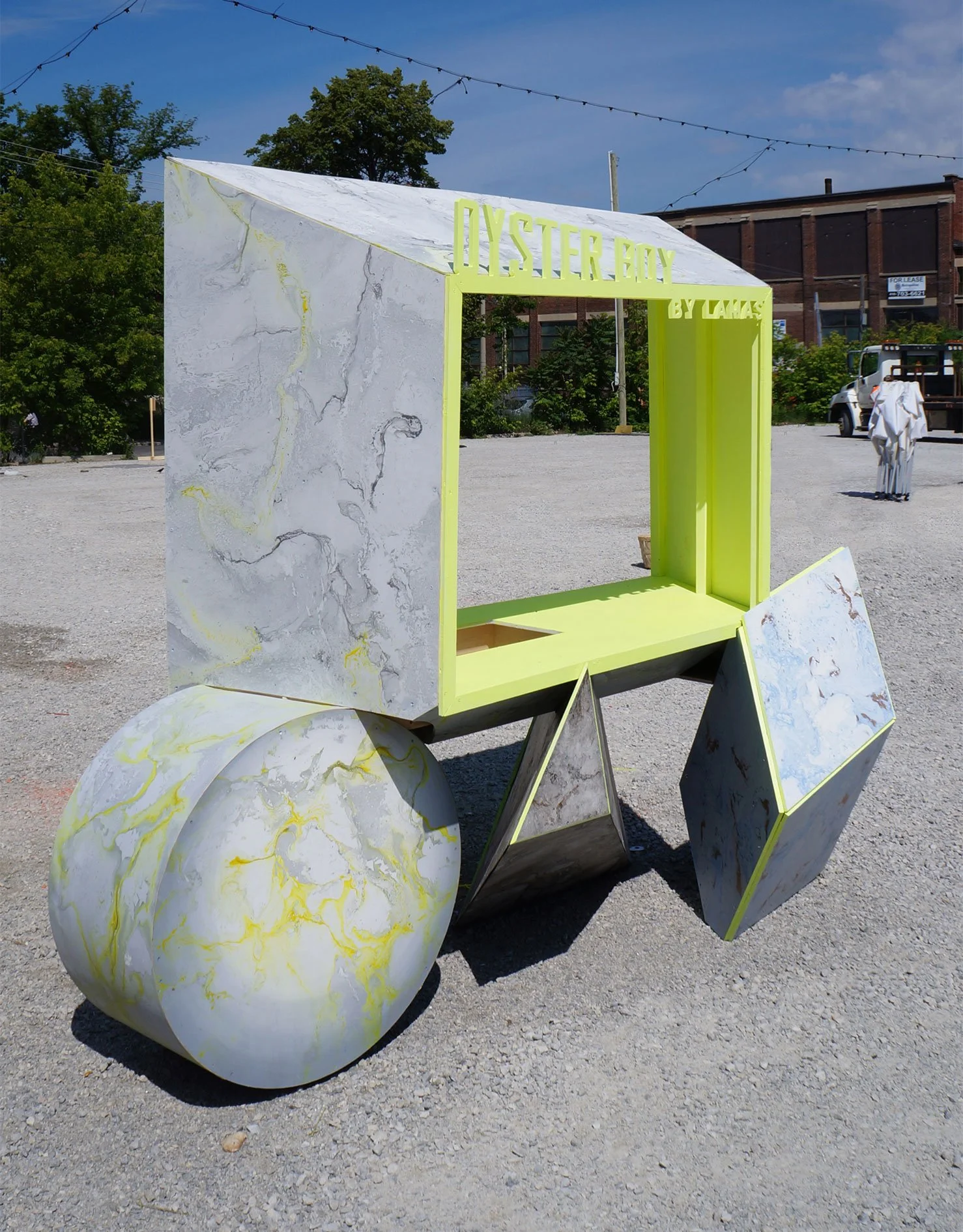 A modern, artistic cart made of marble-like materials with a neon yellow frame, featuring a sign that reads 'OYSTER BOY BY LAIS,' set outdoors on a gravel surface during the daytime.