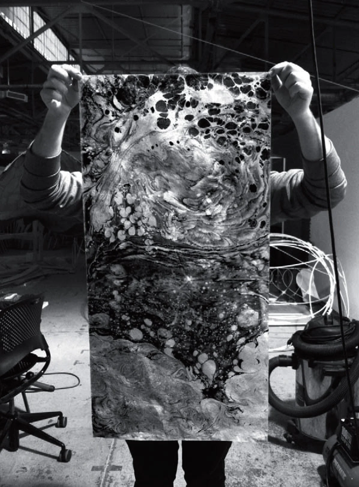 Person holding an abstract black-and-white painting in a warehouse.