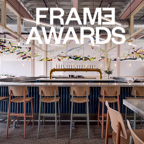 Interior of a modern, industrial-style bar or event space with a navy blue bar counter and wooden chairs, with colorful decorations hanging from the ceiling and large metallic ductwork overhead, promoting the FRAME Awards.
