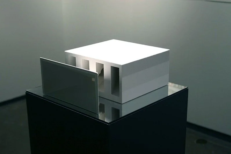 A modern white architectural model with rectangular cutouts displayed on a reflective black pedestal.
