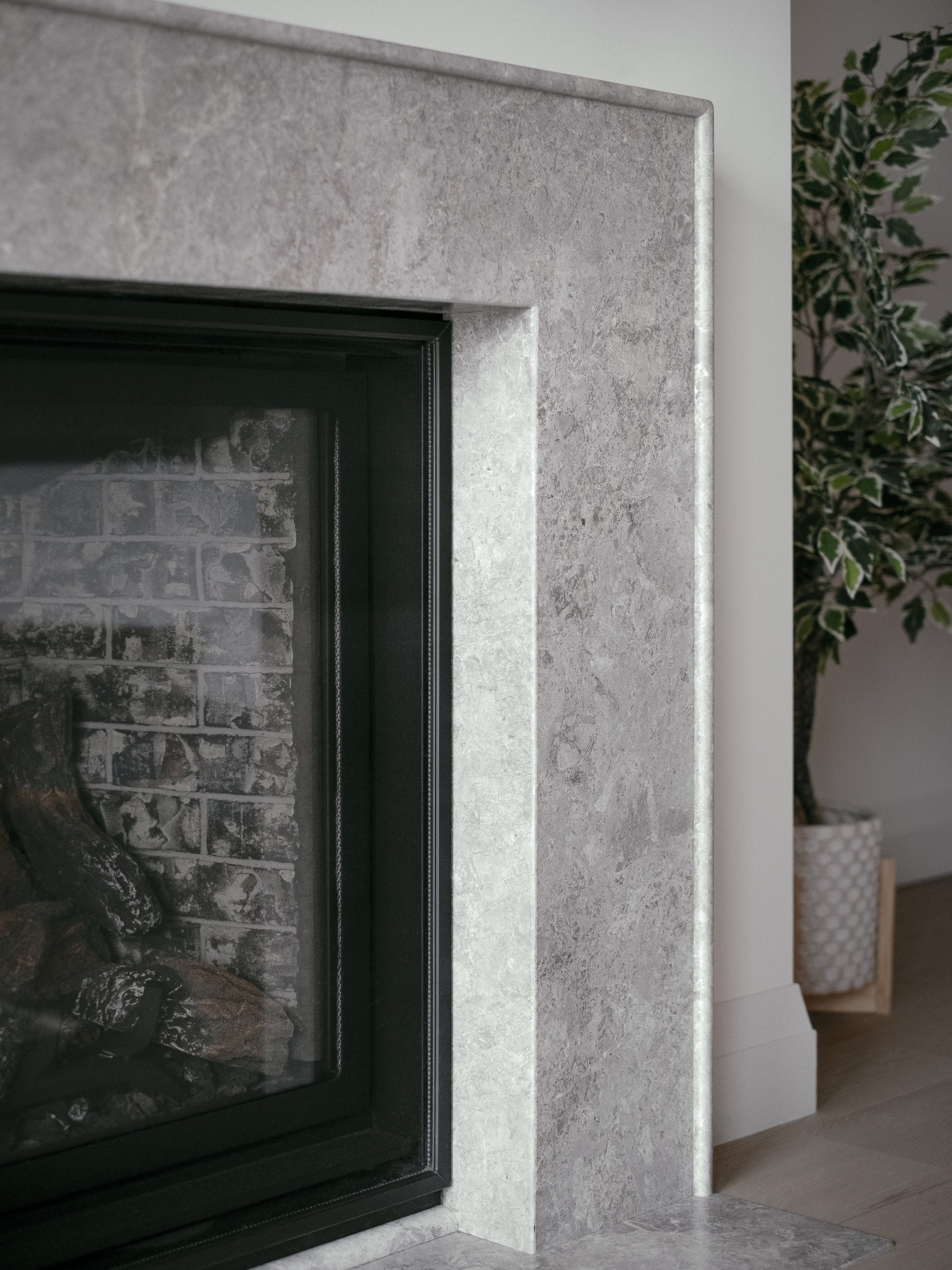 Close-up of a modern fireplace with a black frame, gray stone surround, and wooden house on the interior with a potted plant nearby.