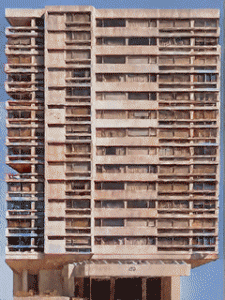A tall, unfinished multi-story building with exposed concrete and numerous balconies.