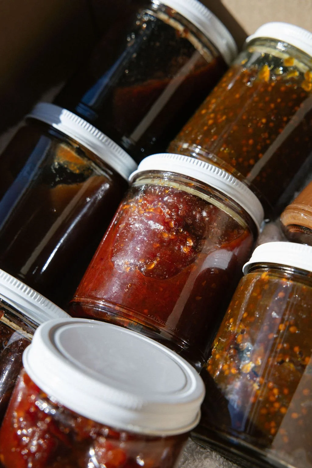 Multiple glass jars filled with homemade chili sauce or hot sauce with visible chili flakes and seeds.