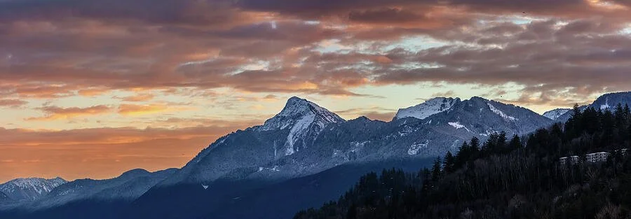 Mountain range with snow-capped peaks under a colorful sunset sky with clouds.