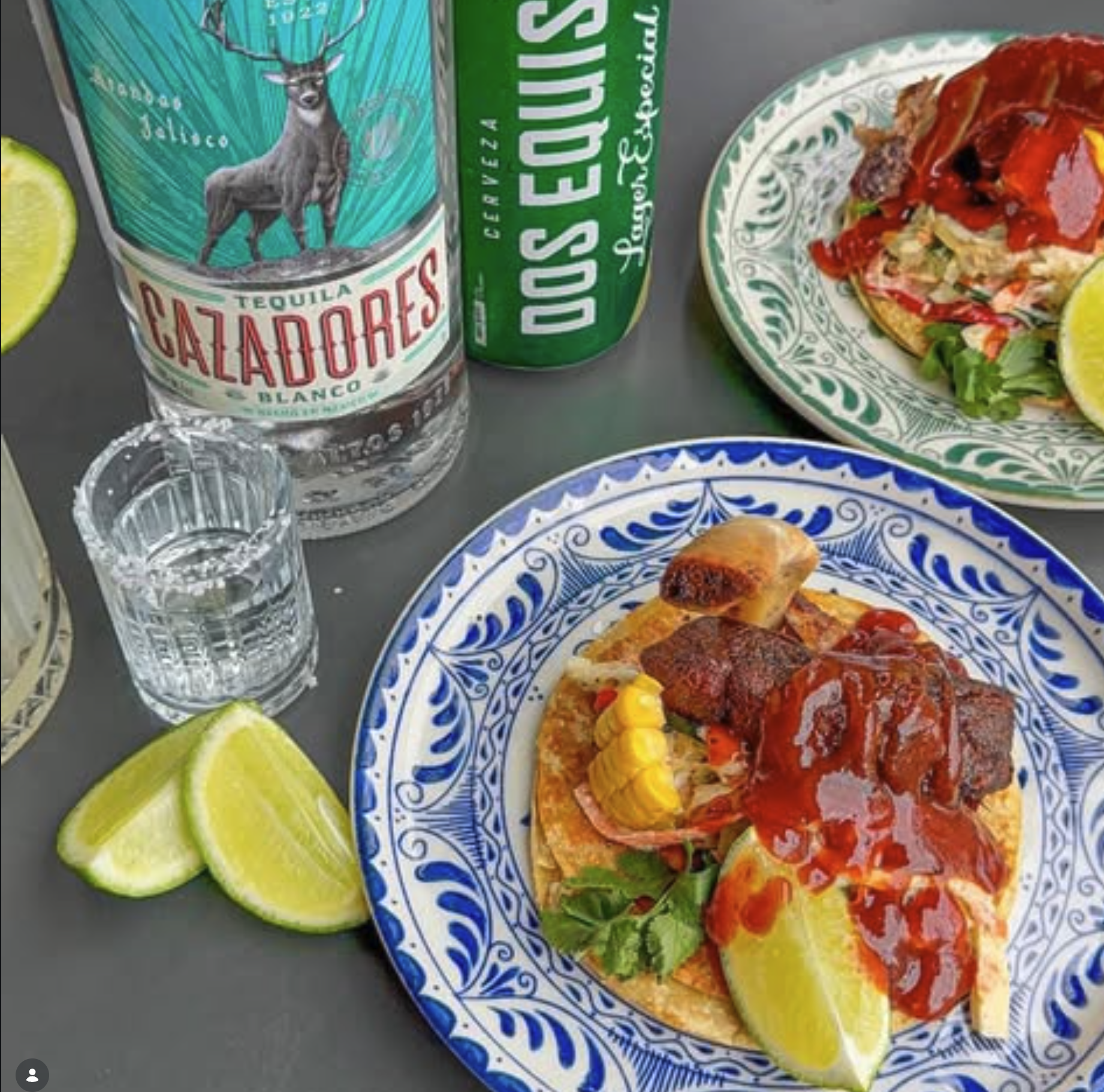 Open Face Tacos on a Mexican designed plate next to a shot of tequila with limes and a bottle of Cazadores tequila