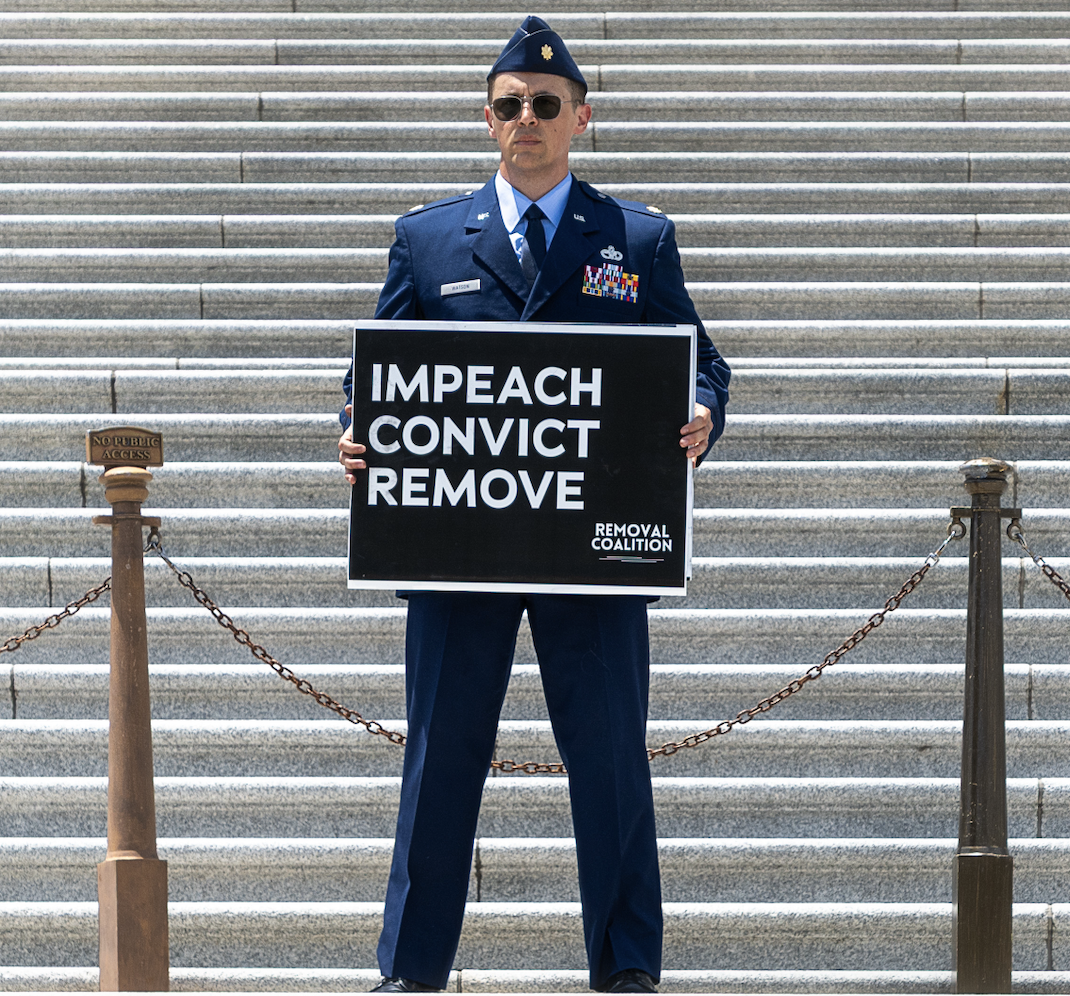 Major Jason Watson stands on the steps holding a sign that reads: Impeach Convict Remove / Removal Coalition.  Photo by Matthew Wagner.