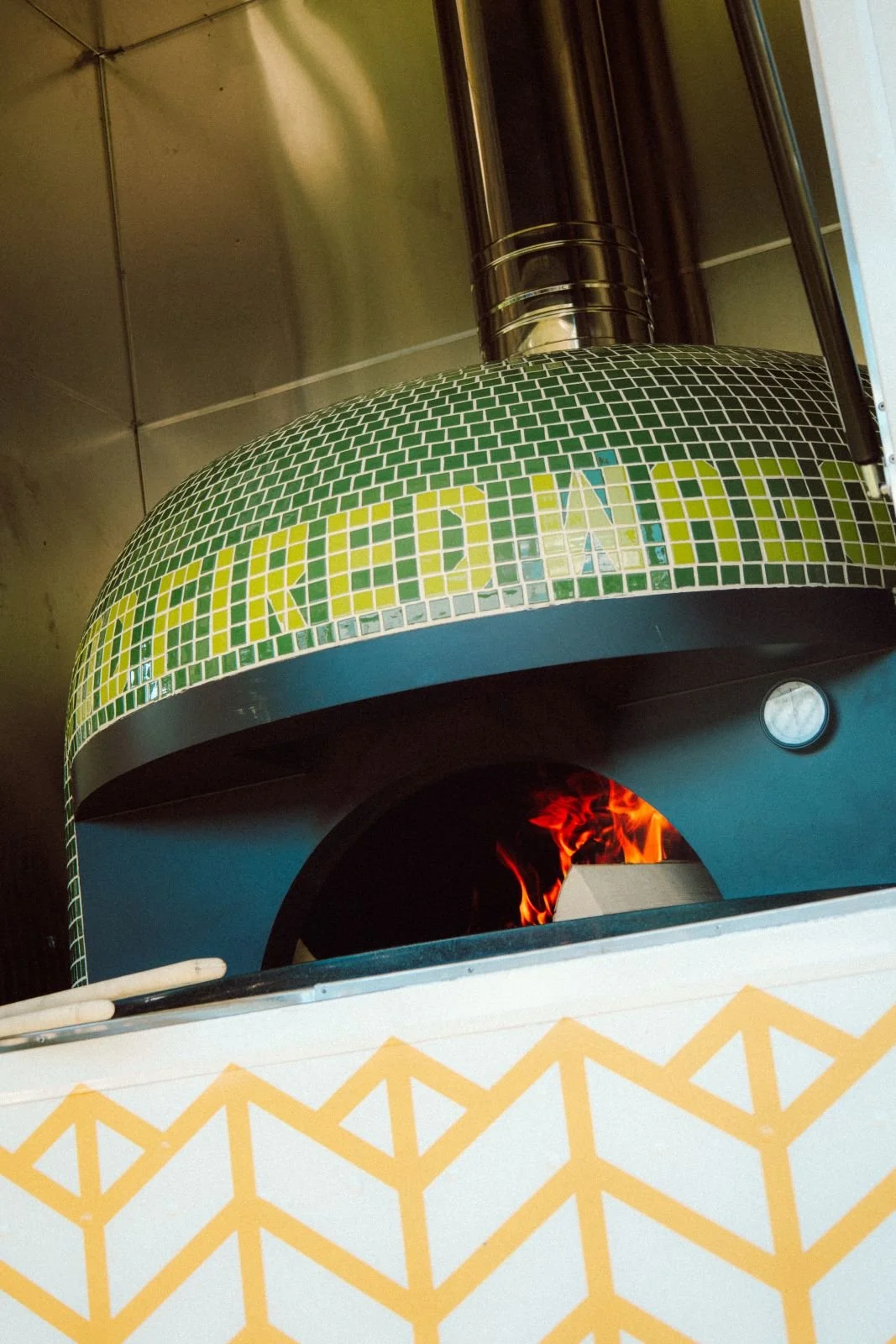 A wood fired pizza oven with green mosaic tiles, fired up for a night of authentic wood fired pizzas , entrees, appetixers and so much more.