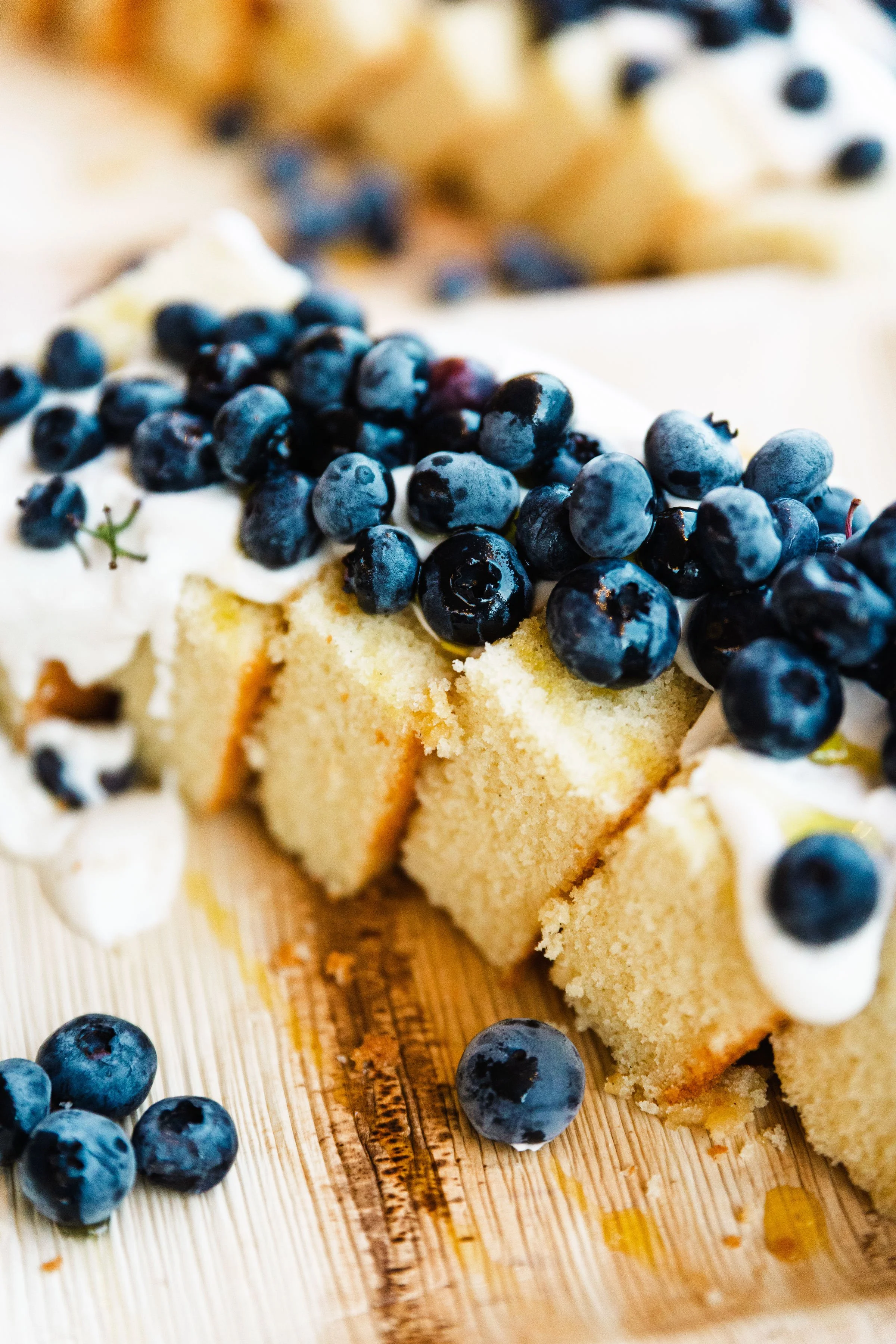 Close-up of a partially sliced vanilla sponge cake topped with blueberries and whipped cream on a wooden surface.