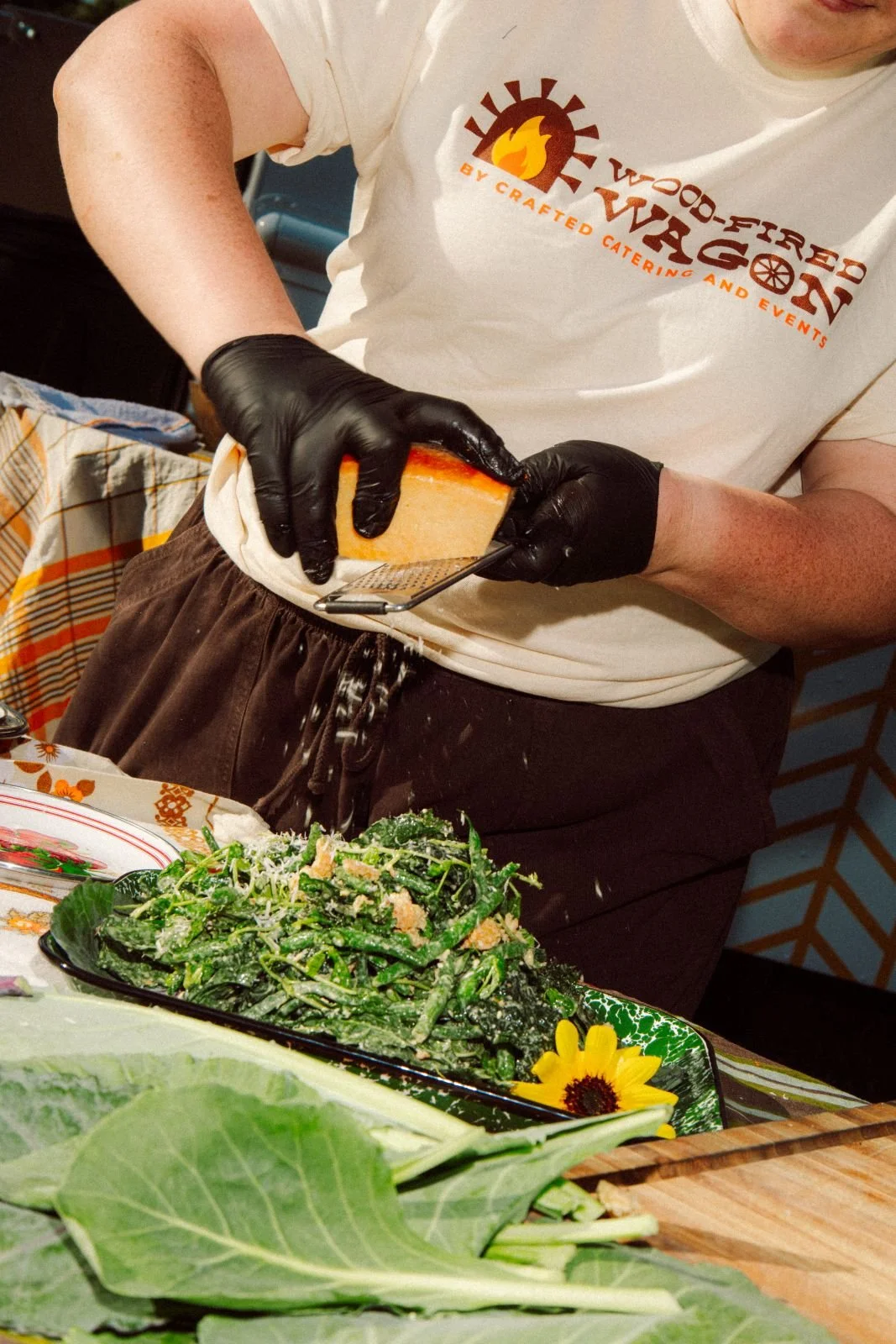 Person wearing black gloves grating cheese over a green salad at a festive gathering.