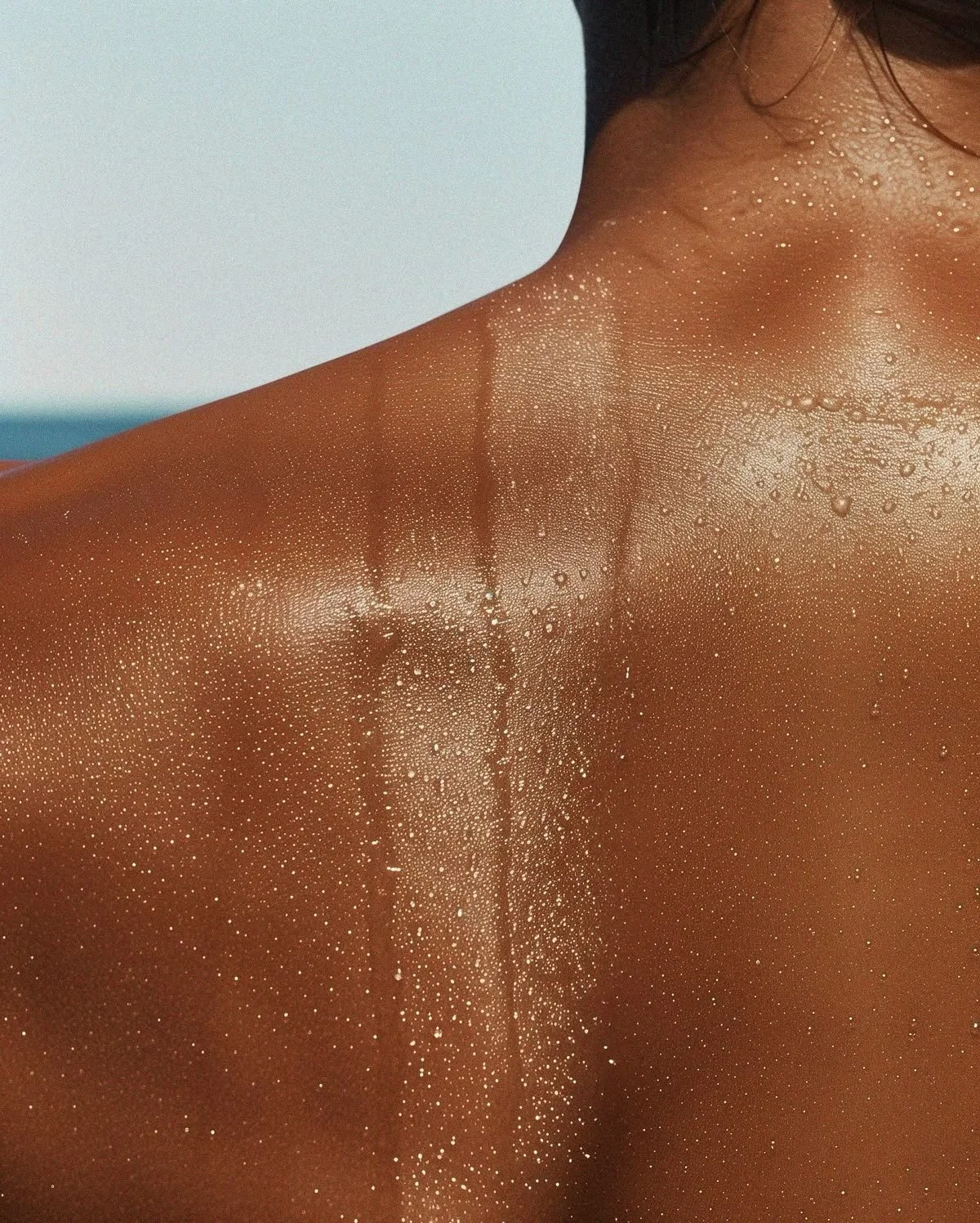 Close-up of a person with water droplets on their shoulder and neck, with a backdrop of blue sky.